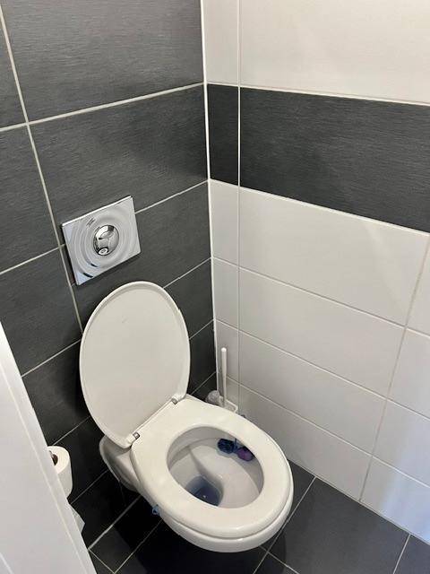 Wandhängende Toilette mit moderner Spülplatte in einem gefliesten Gäste-WC.