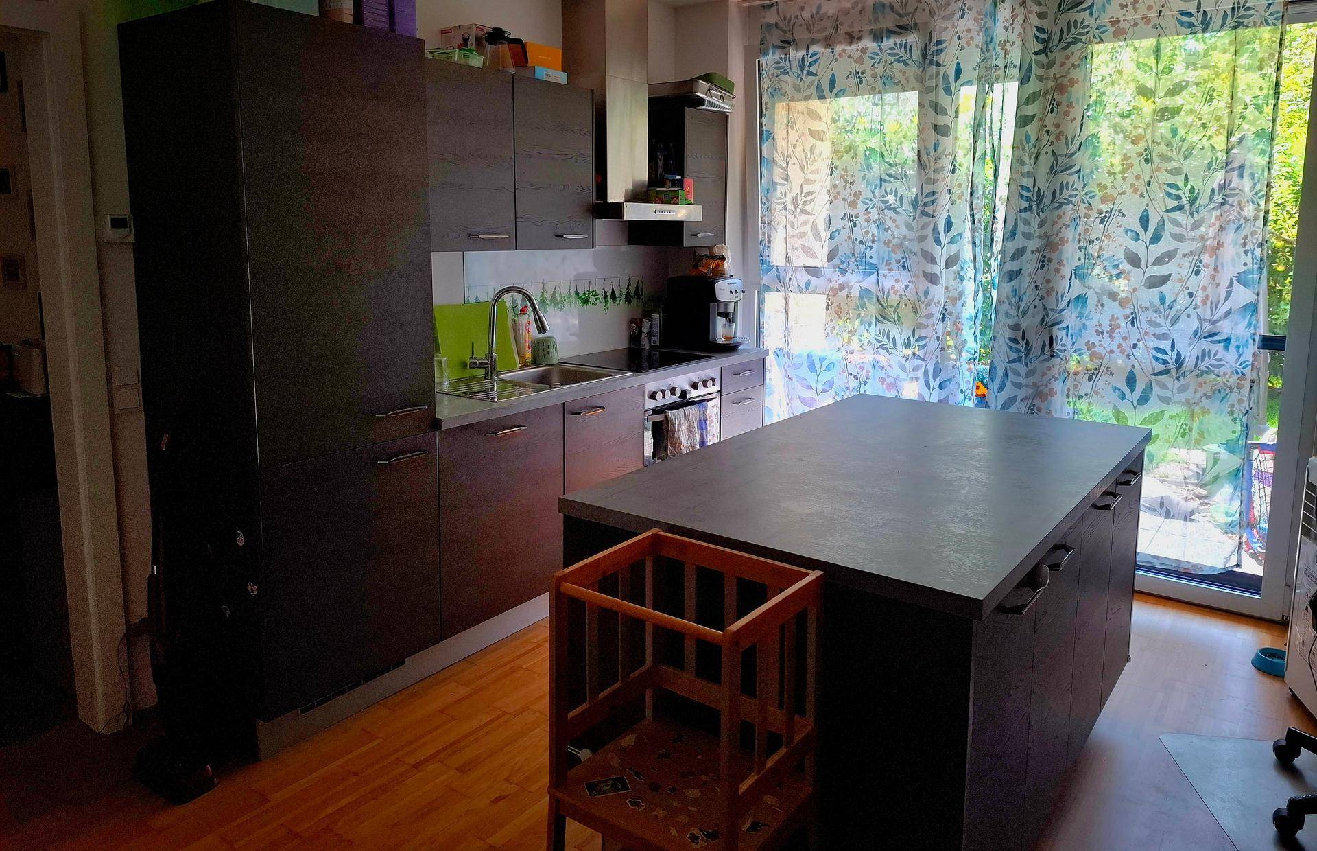Moderne Küche mit dunklen Schränken, Kücheninsel und Zugang zum Balkon oder Garten.