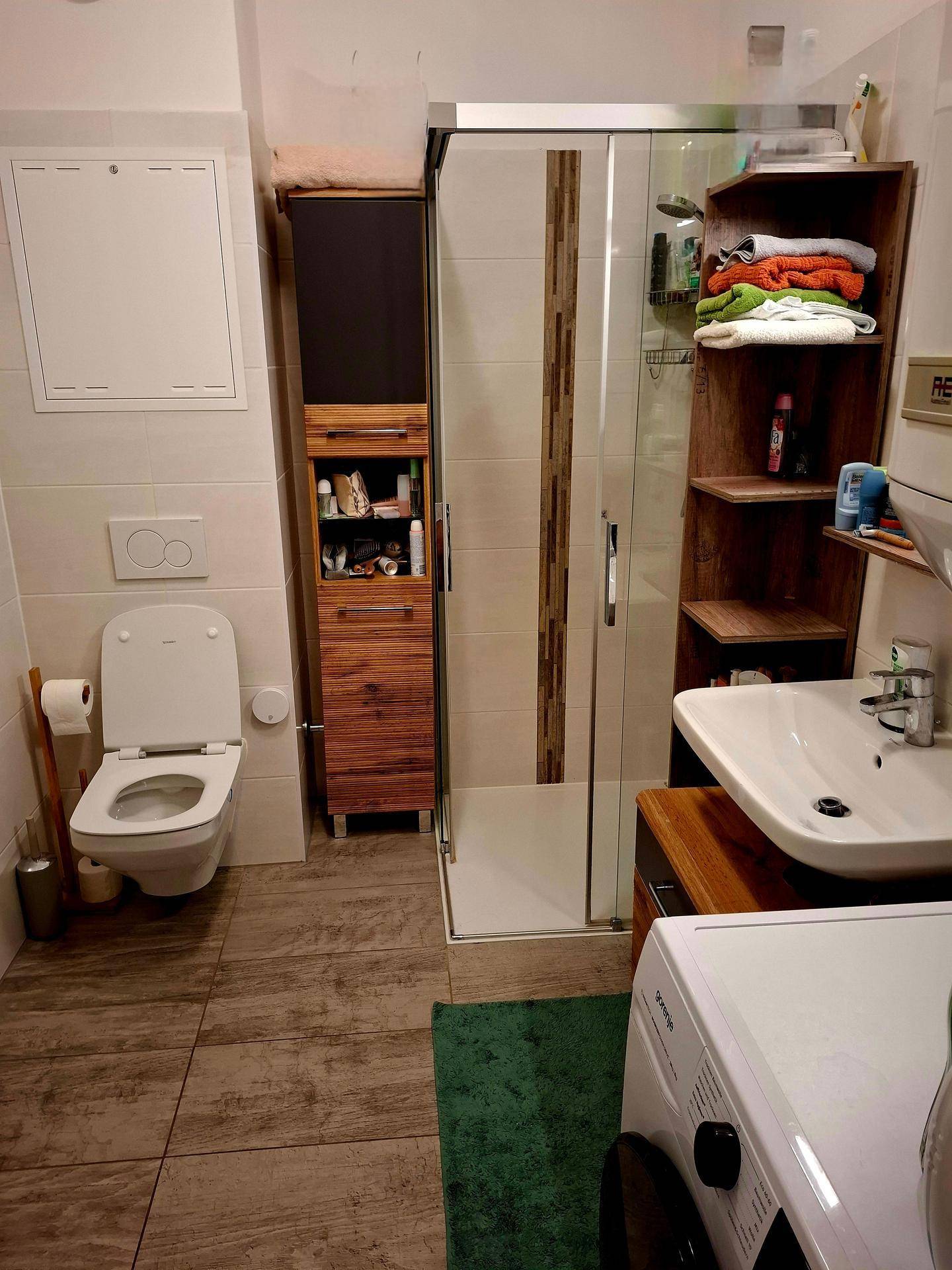 Modernes Badezimmer mit Dusche, WC und Waschbecken, gefliest in neutralen Farben.