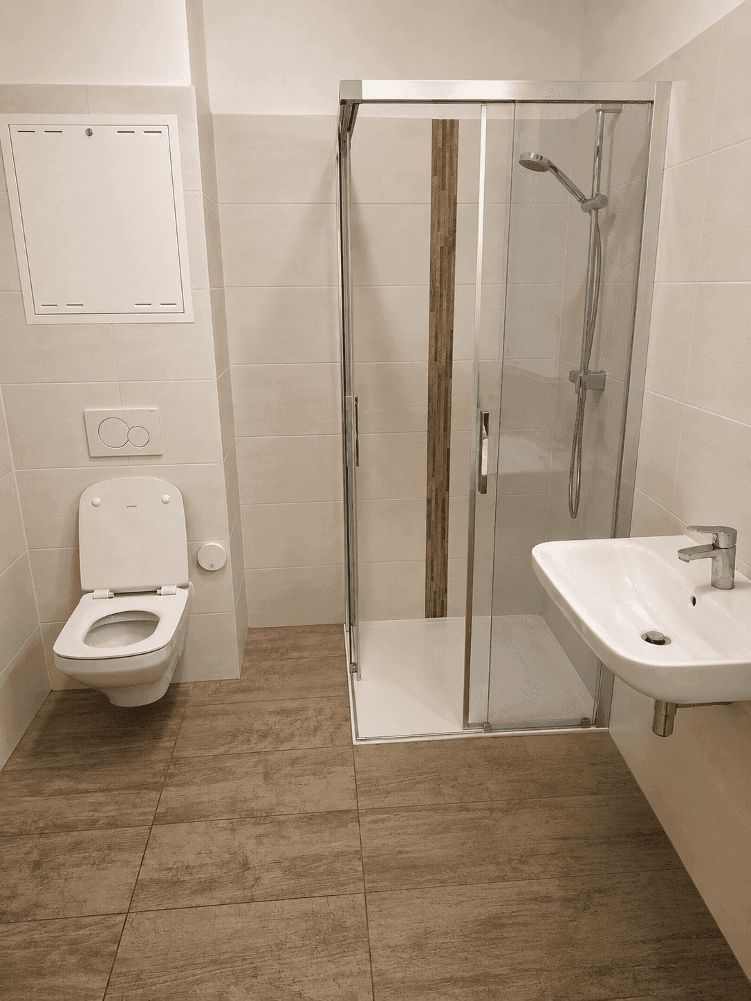 Helles Badezimmer mit Dusche, WC und Waschbecken, gefliest in warmen Farbtönen.