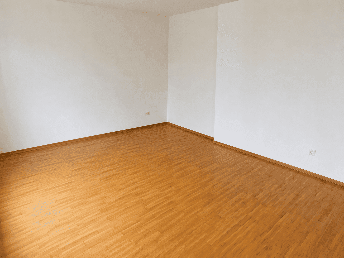 Leeres Zimmer mit Holzboden und weißen Wänden, bietet viel Platz für individuelle Gestaltung.