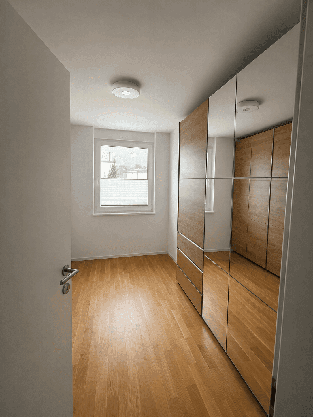 Helles Zimmer mit großem Spiegelschrank und hellem Parkettboden.