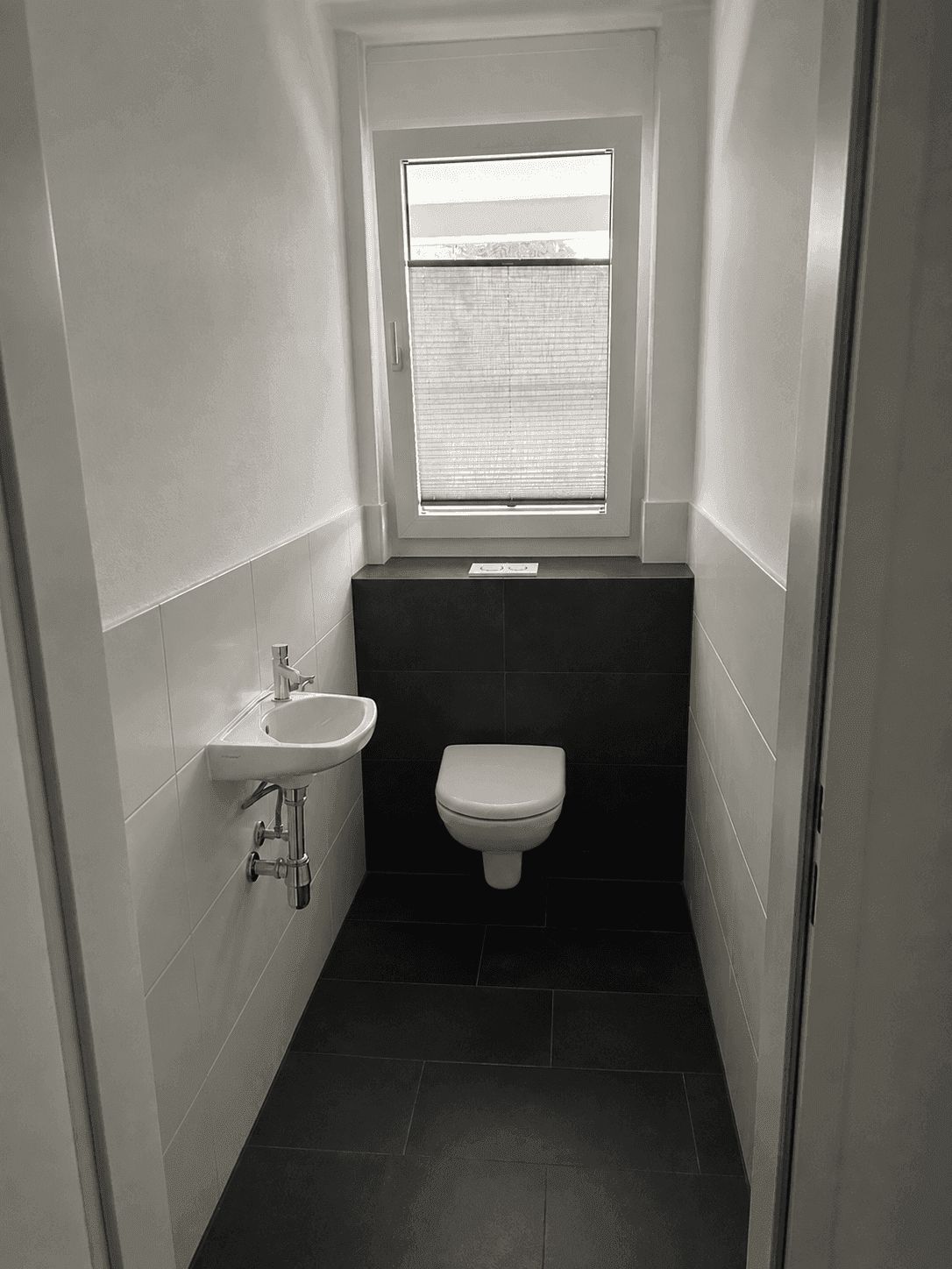Gäste-WC mit wandhängender Toilette, kleinem Waschbecken und Fenster.