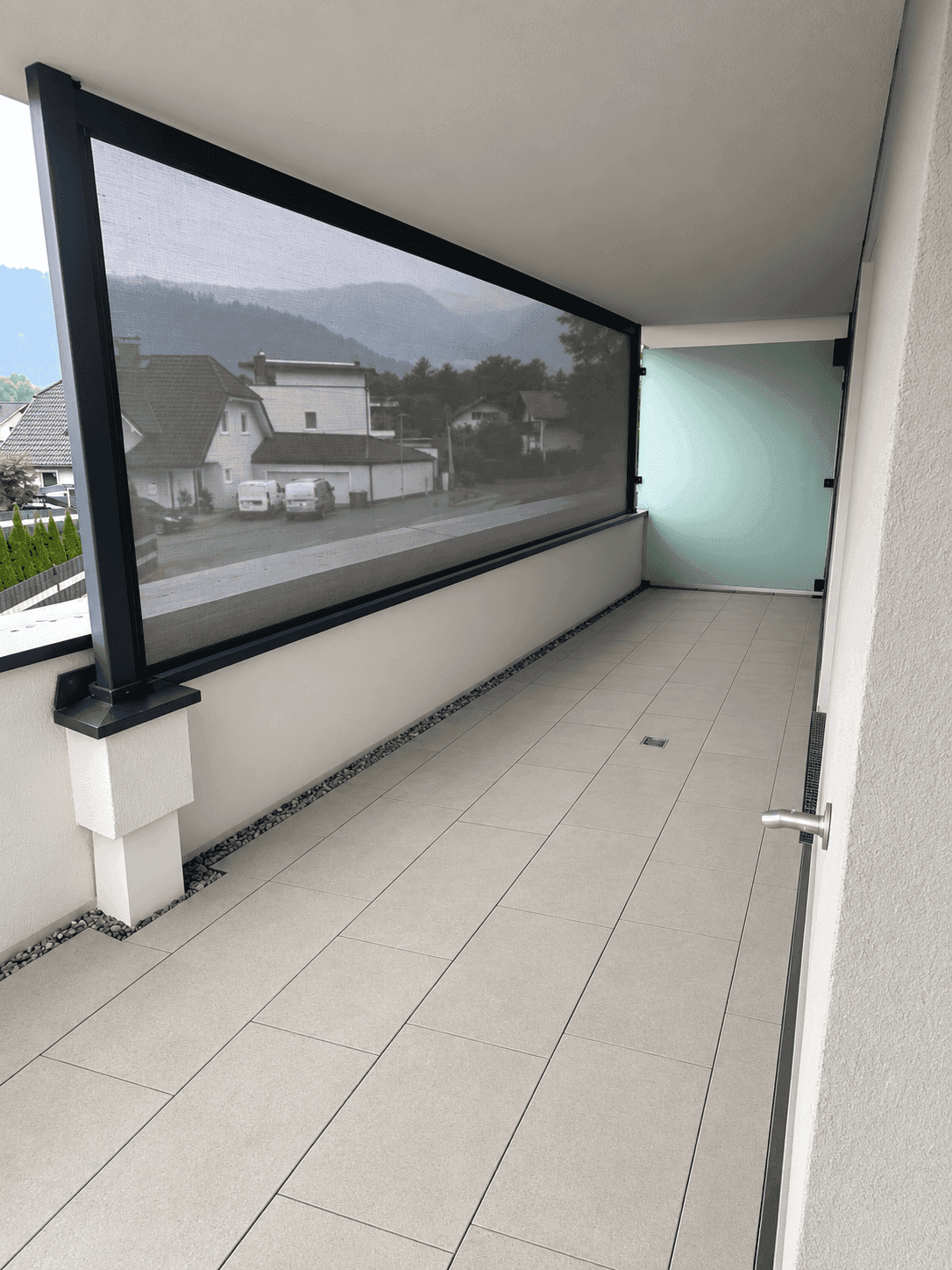 Moderner Balkon mit Fliesenboden, Sichtschutz und Bergblick.