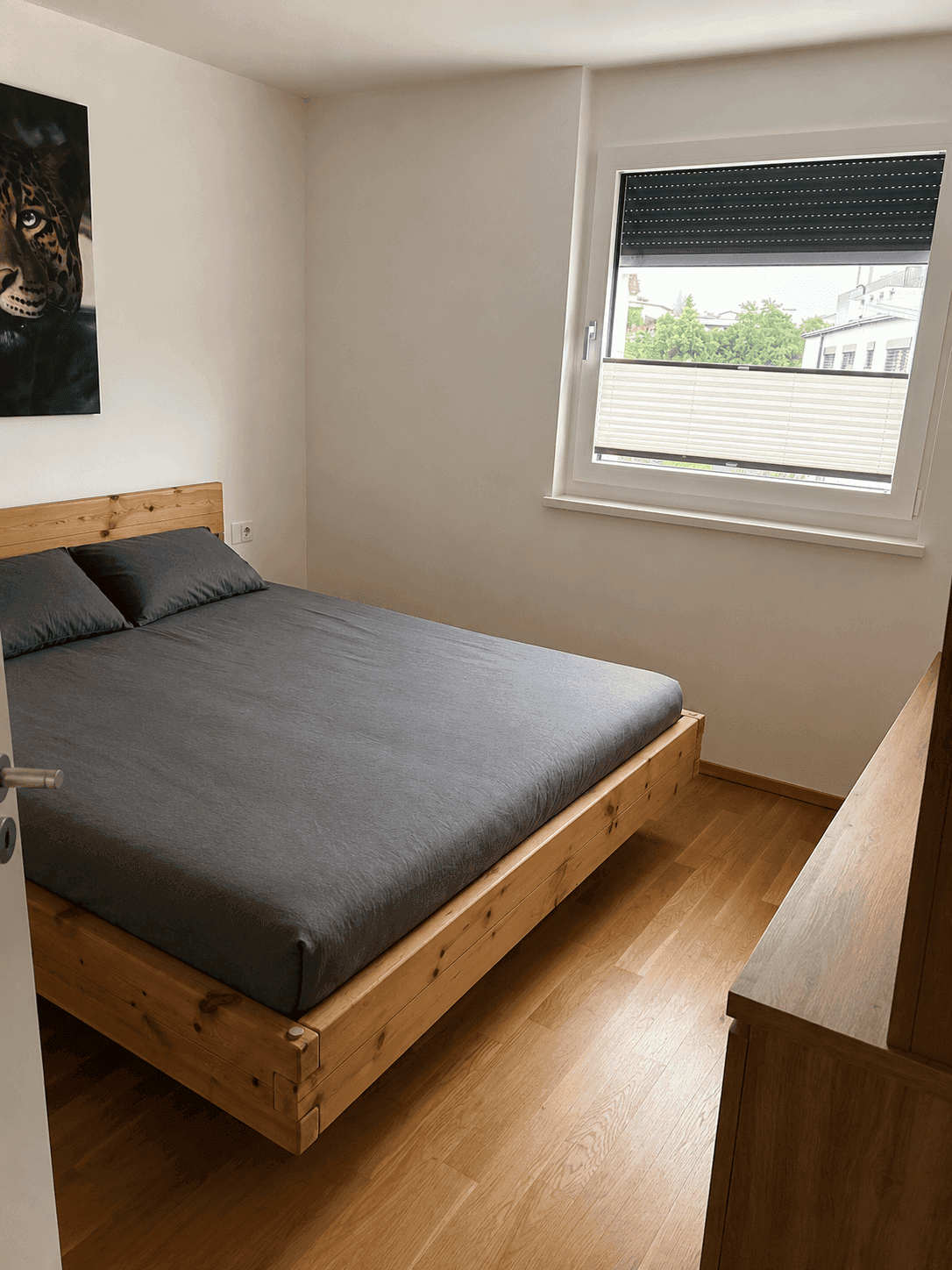 Schlafzimmer mit hellem Holzbett, Parkettboden und Fenster mit Rollladen.