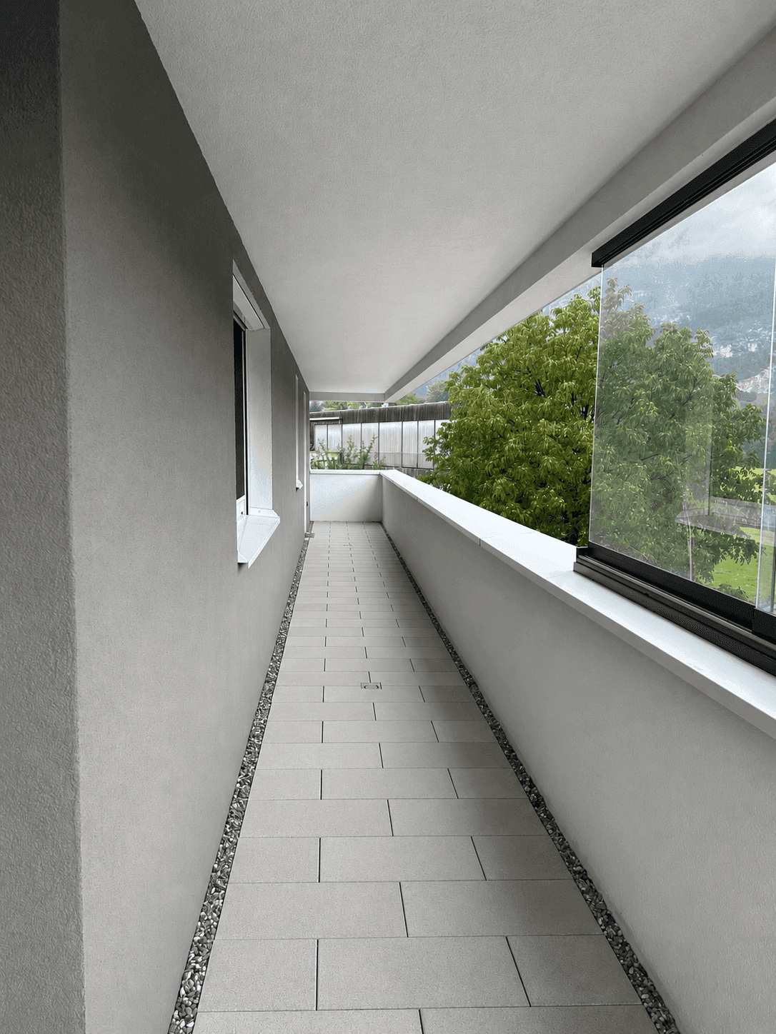 Langer, schmaler Balkon mit Fliesenboden und Blick ins Grüne.