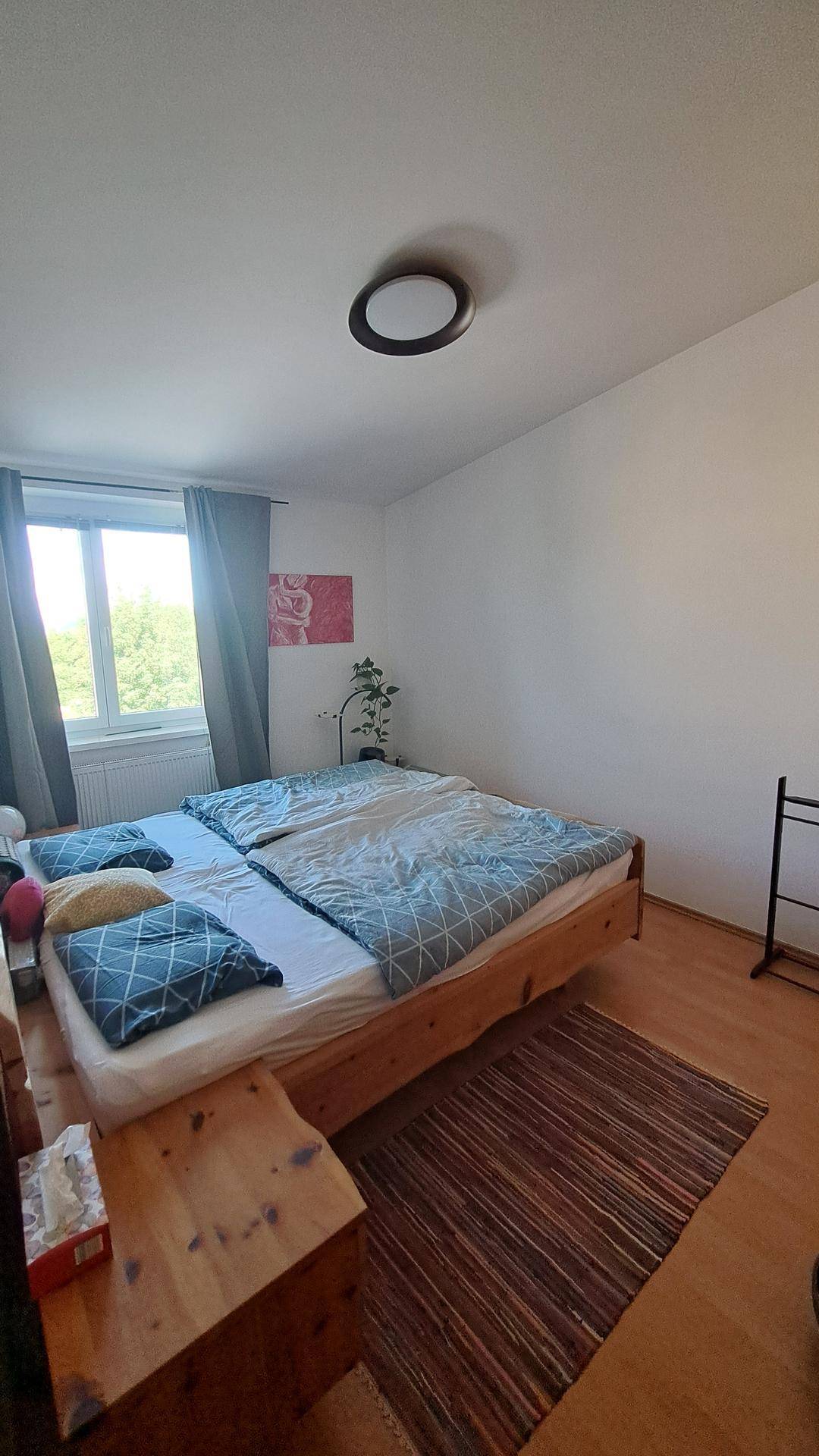 Gemütliches Schlafzimmer mit Doppelbett, Holzboden und Fenster mit Blick ins Grüne.