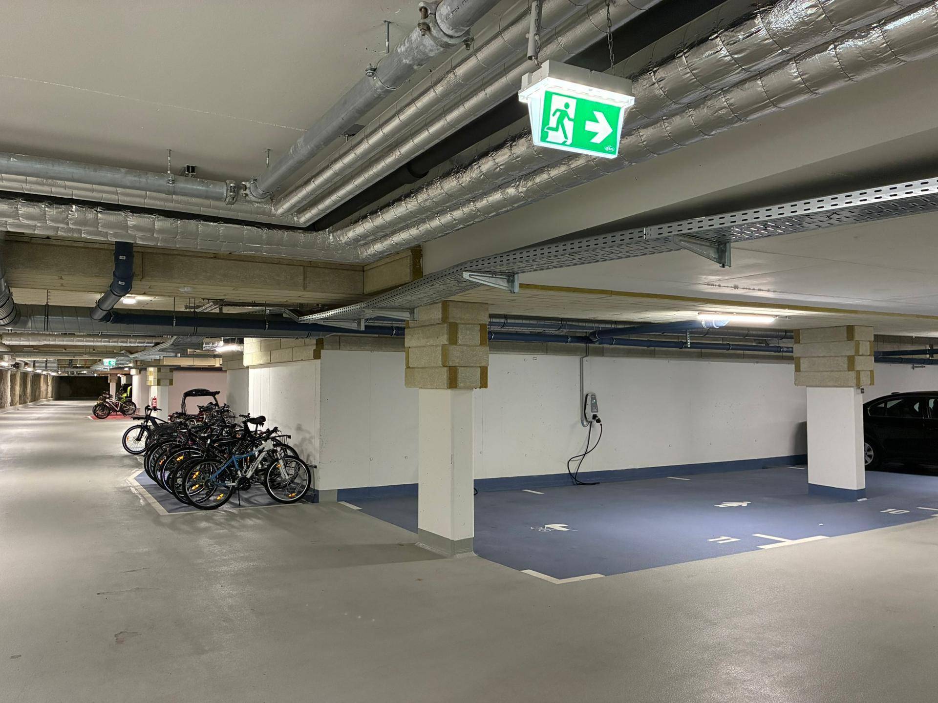 Tiefgarage mit Fahrradabstellplätzen, freiliegenden Leitungen und Ladestation für Elektrofahrzeuge.
