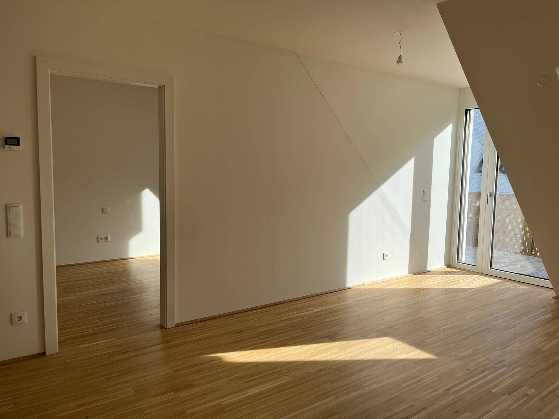 Lichtdurchfluteter Wohnraum mit Holzboden, Dachschräge und Zugang zu einem Außenbereich.