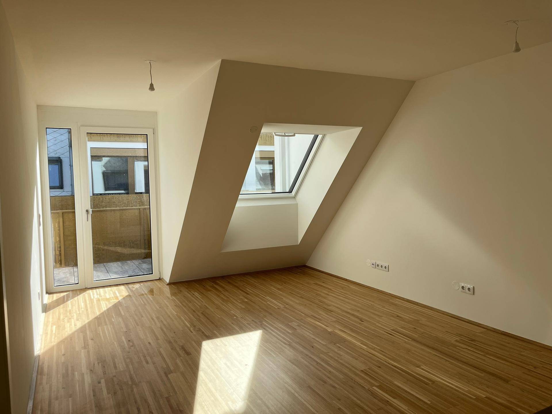 Geräumiger Wohnraum mit Holzboden, Dachschräge, Dachfenster und Balkonzugang.
