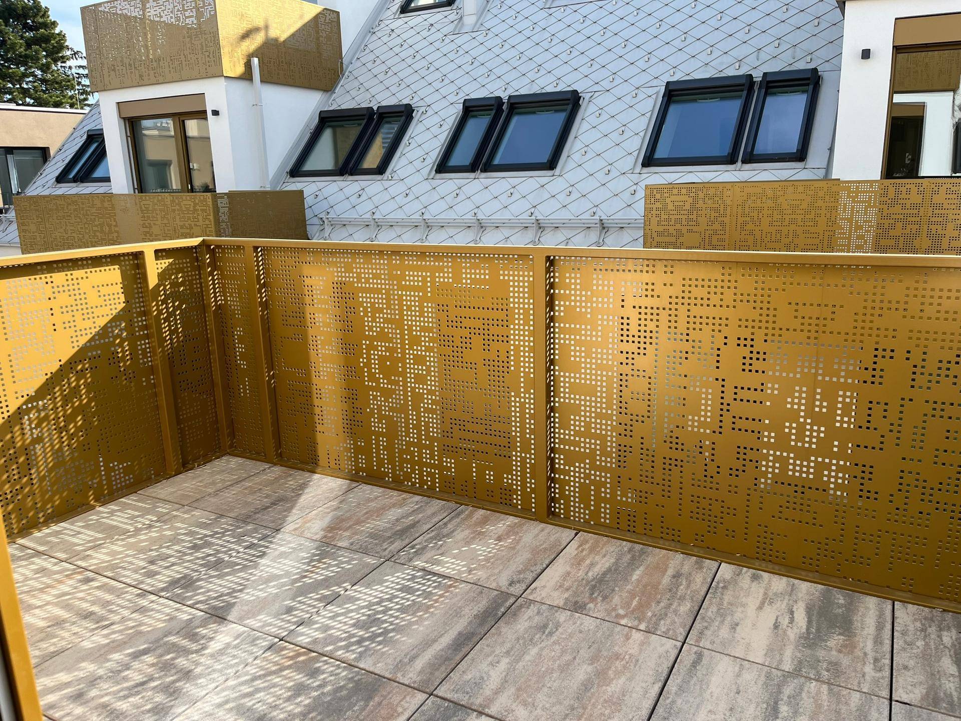 Moderner Balkon mit perforiertem Metallgeländer und Fliesenboden, Blick auf das Dach.