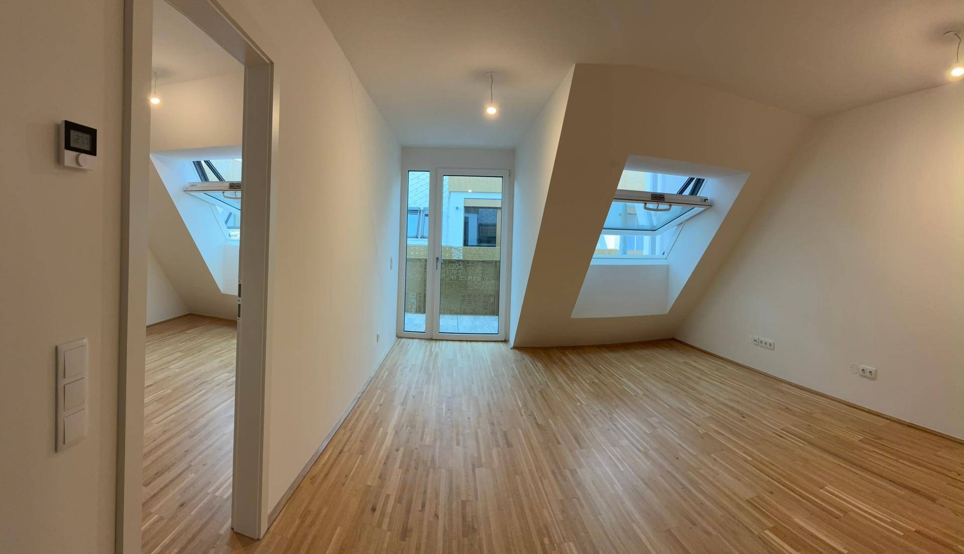 Heller Wohnraum mit Holzboden, Dachschrägen und Zugang zu einem Balkon.
