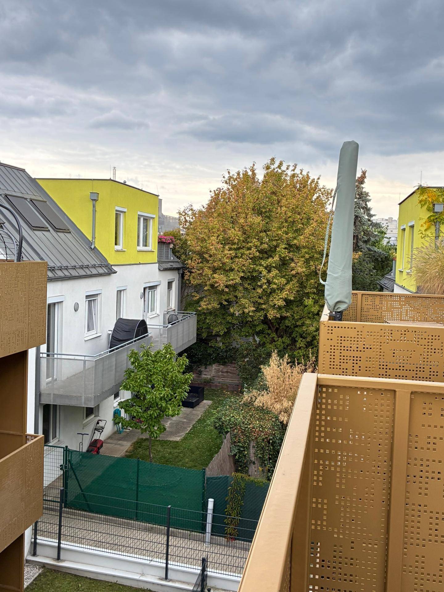 Blick vom Balkon auf einen grünen Innenhof mit Bäumen und umliegenden Gebäuden.