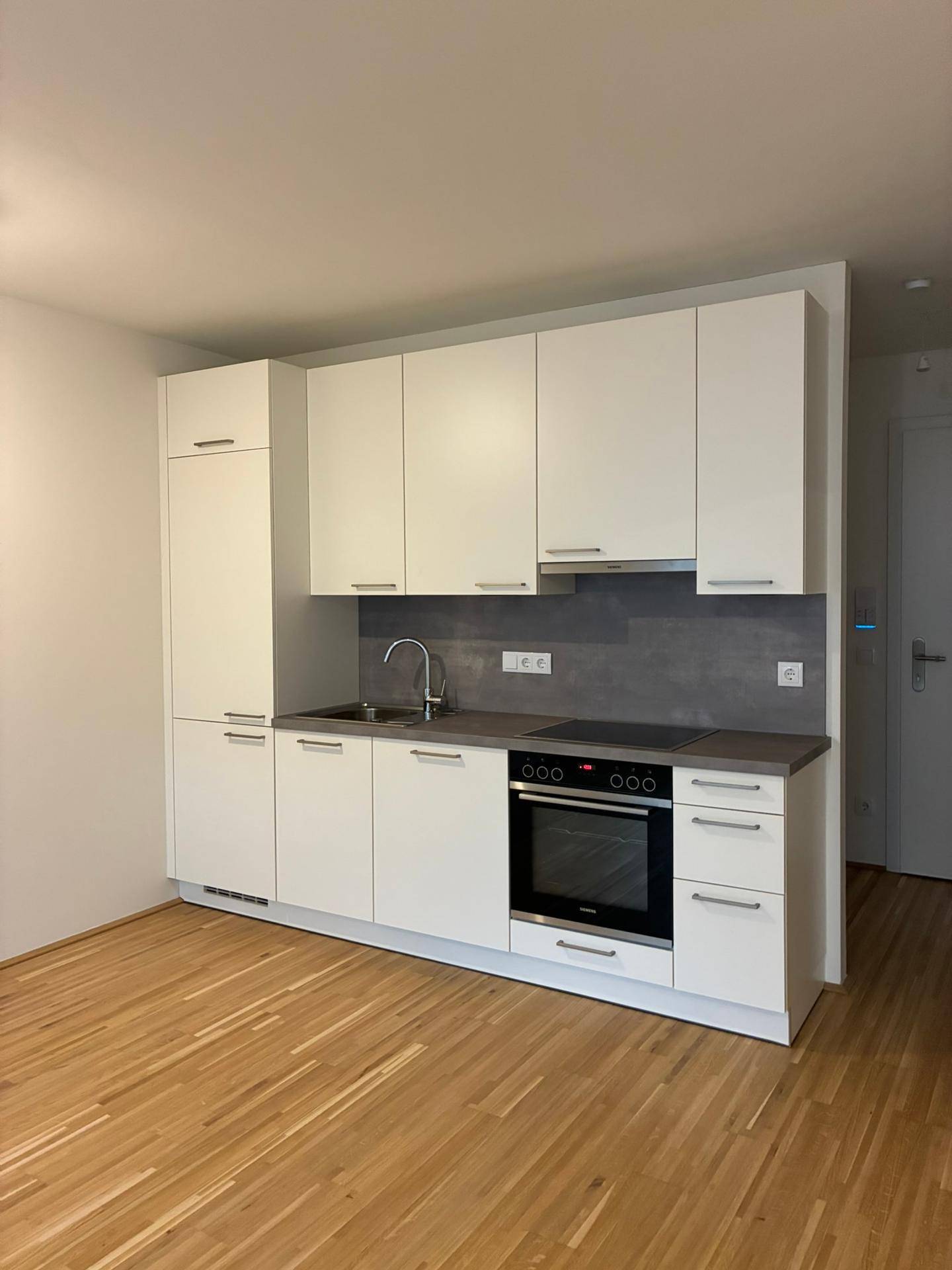 Moderne Küchenzeile mit weißen Schränken, integrierten Geräten und Holzboden.