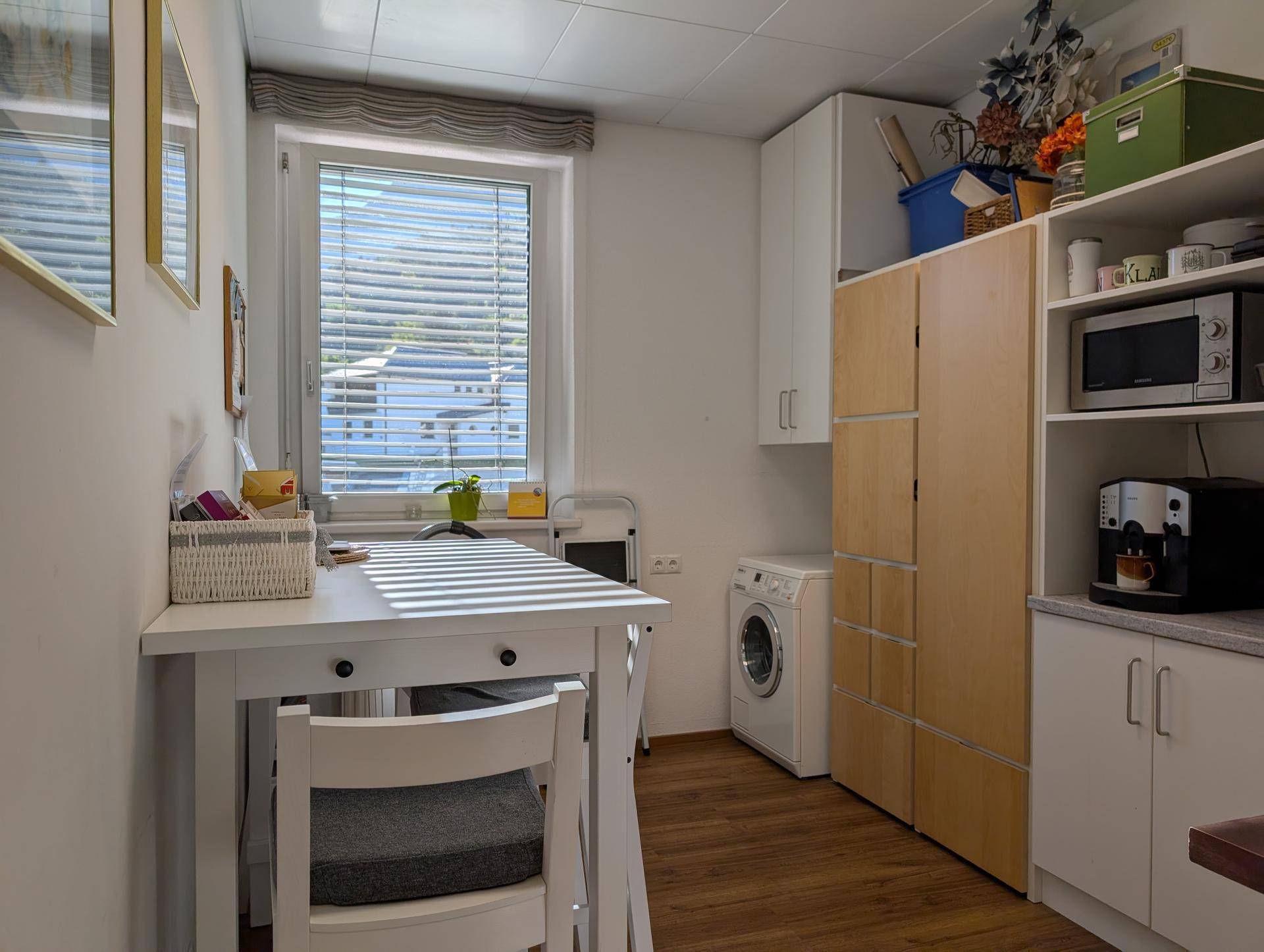 Helle Küchenzeile mit Esstisch, Waschmaschine und Fenster, das viel Tageslicht hereinlässt.