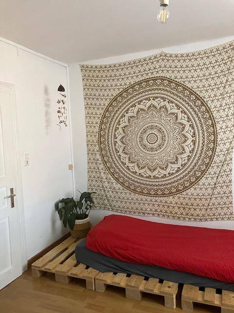 Gemütliches Schlafzimmer mit Palettenbett, Wandteppich und Holzboden.
