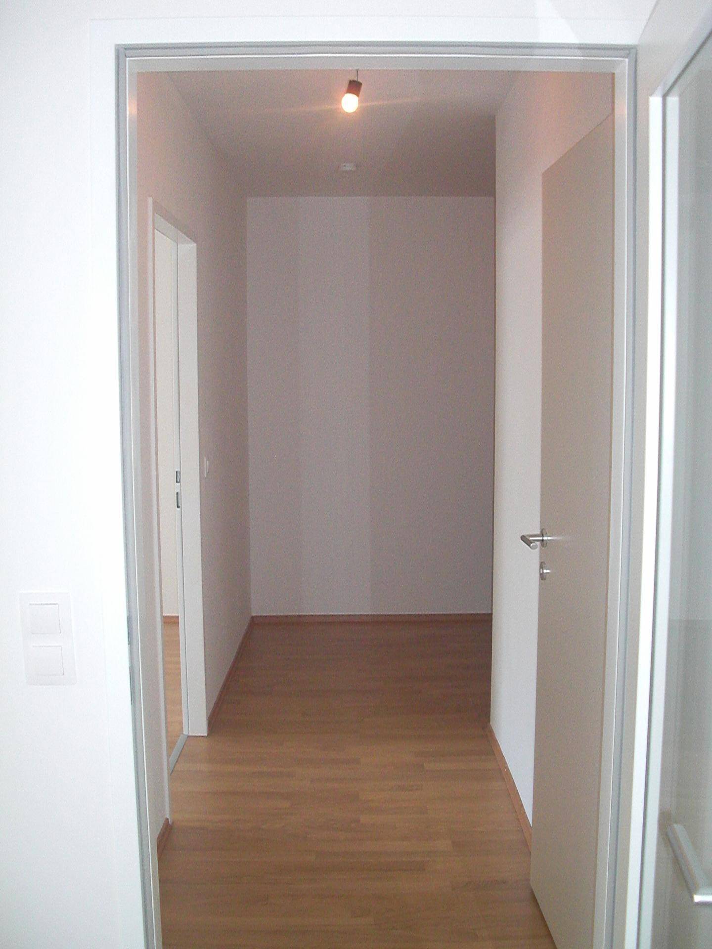 Heller Flur mit Holzboden und weißen Wänden, der zu weiteren Räumen führt.