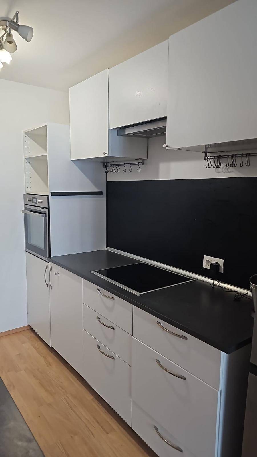 Helle Küche mit Induktionskochfeld, Backofen und weißen Schränken.