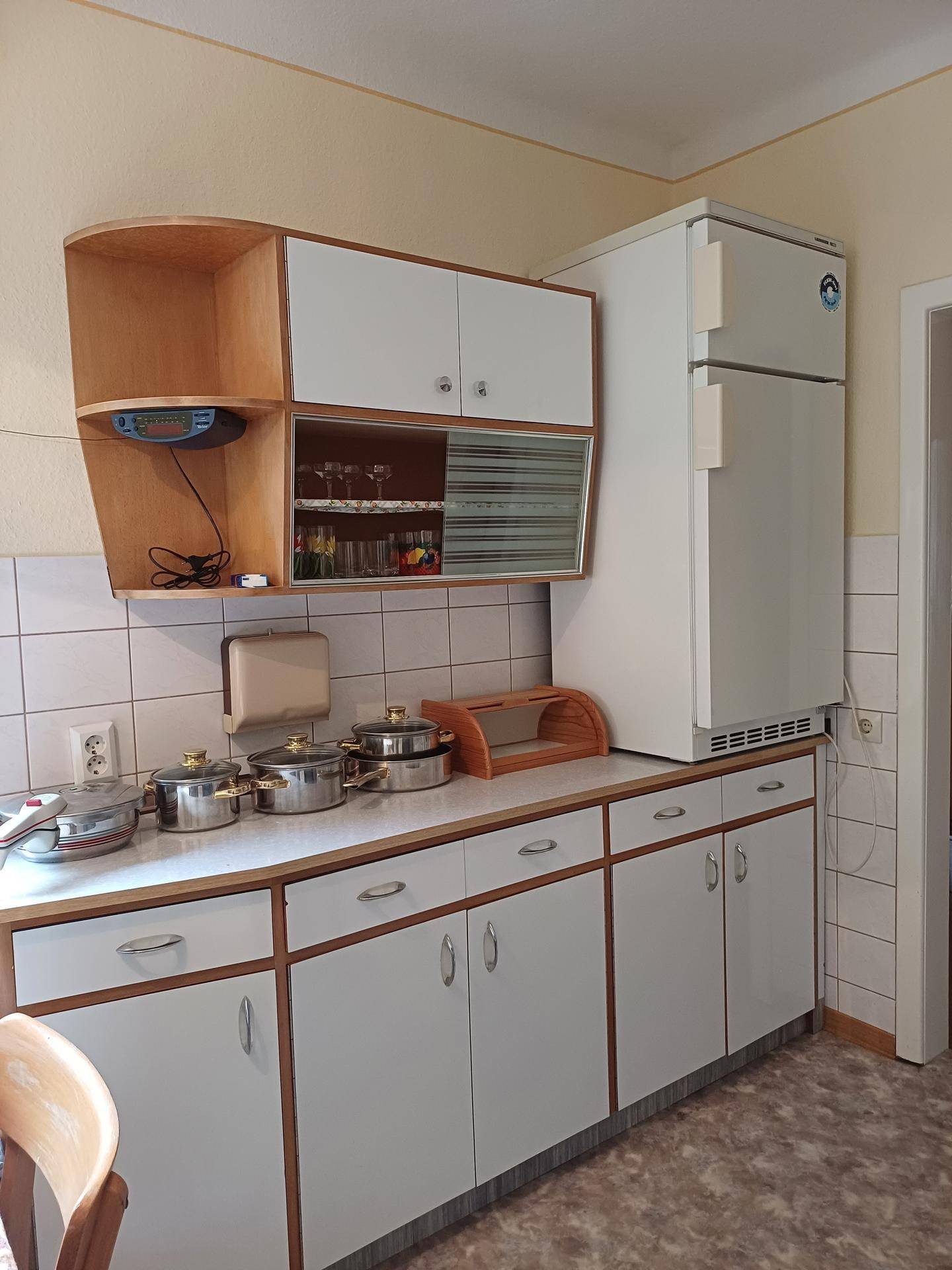 Ältere Küche mit weißen Schränken, Kühlschrank und viel Stauraum.