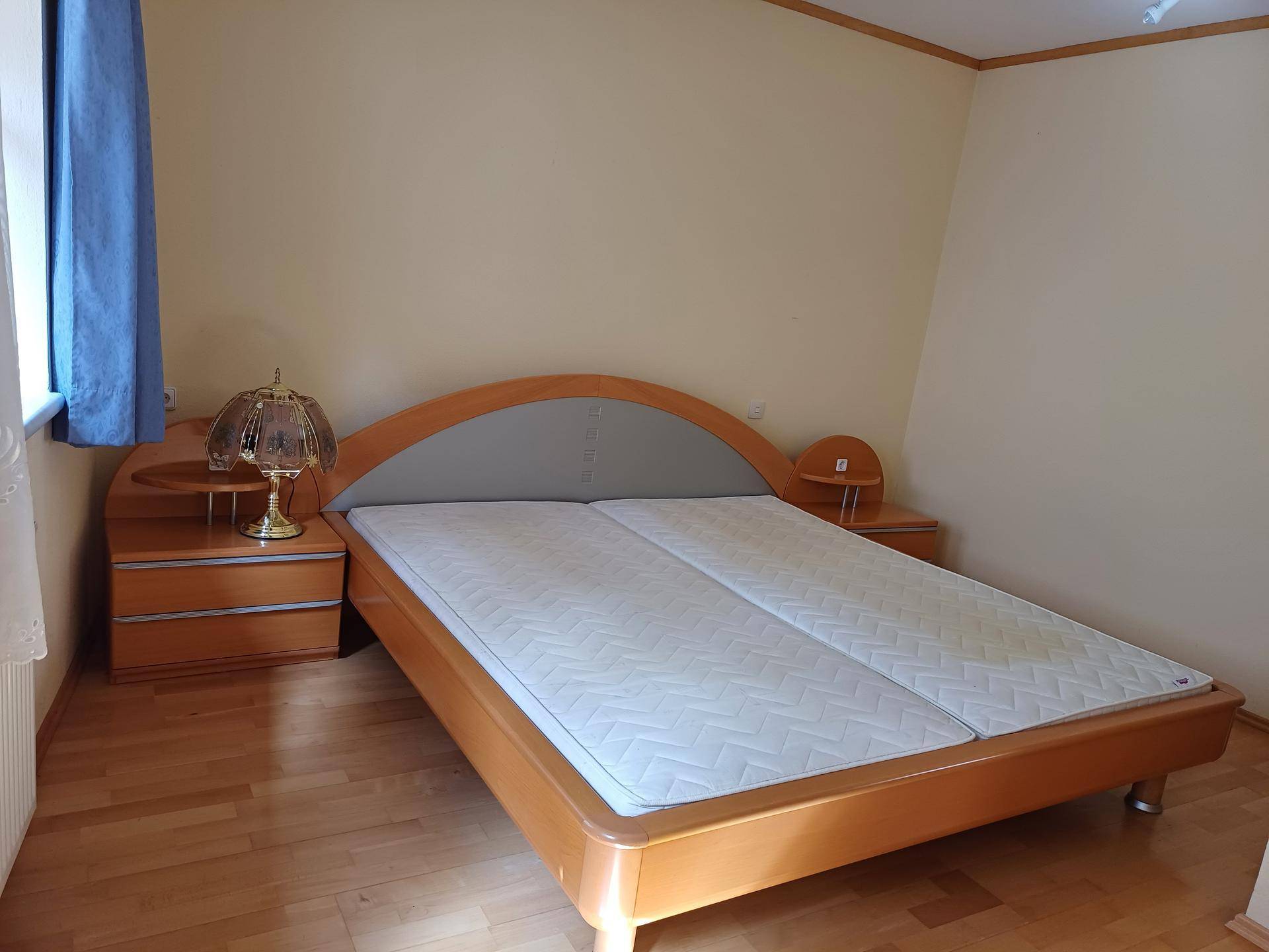 Schlafzimmer mit Doppelbett aus hellem Holz, Nachttischen und Parkettboden.