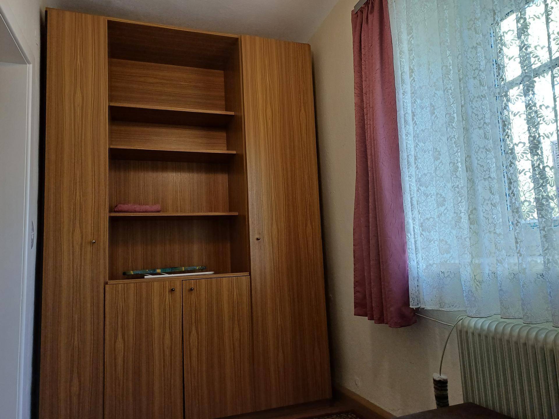Schlafzimmer mit großem Holzschrank, Fenster und Vorhängen.