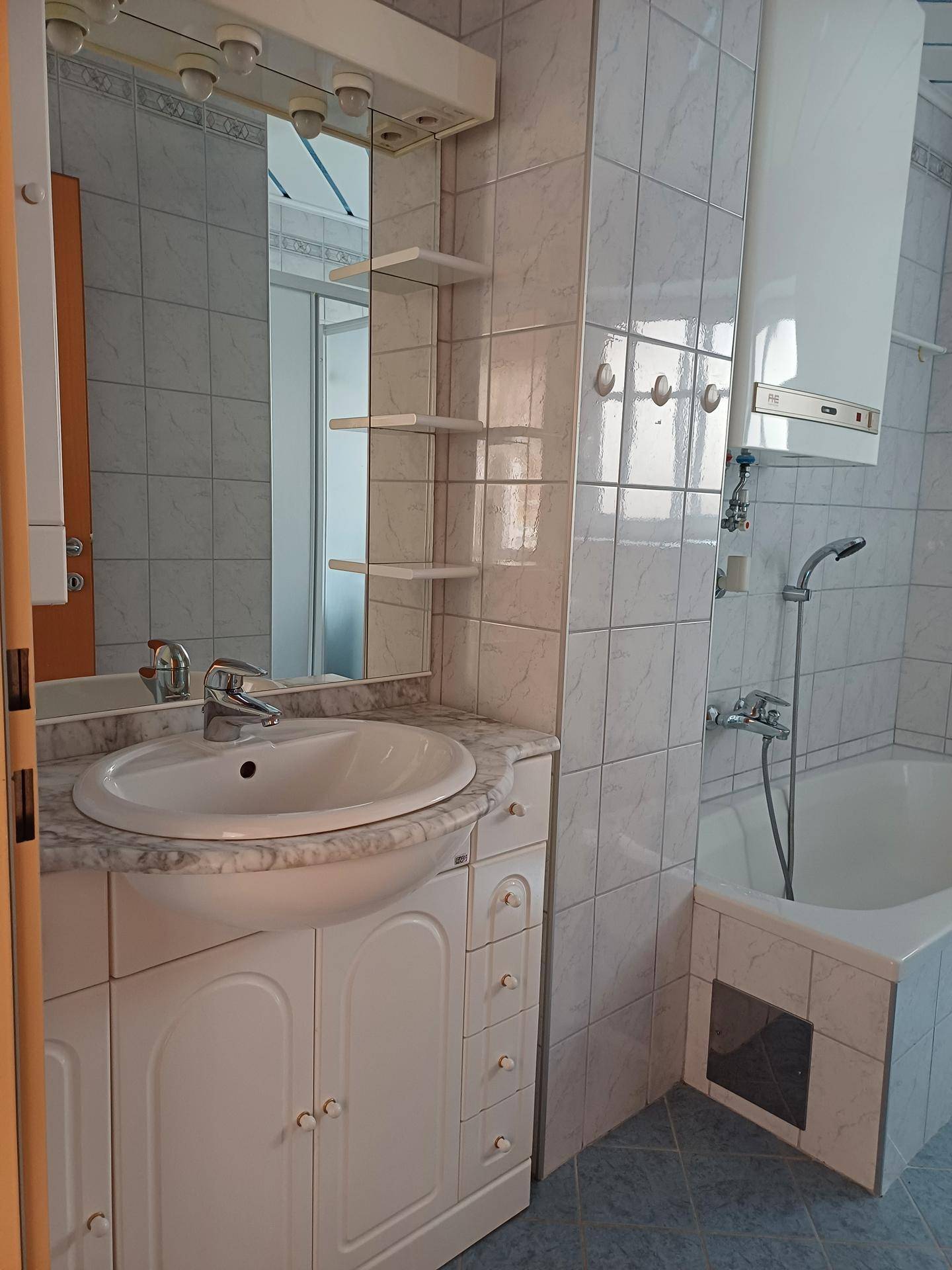 Badezimmer mit Waschbecken, Spiegelschrank und Badewanne mit Duscharmatur.