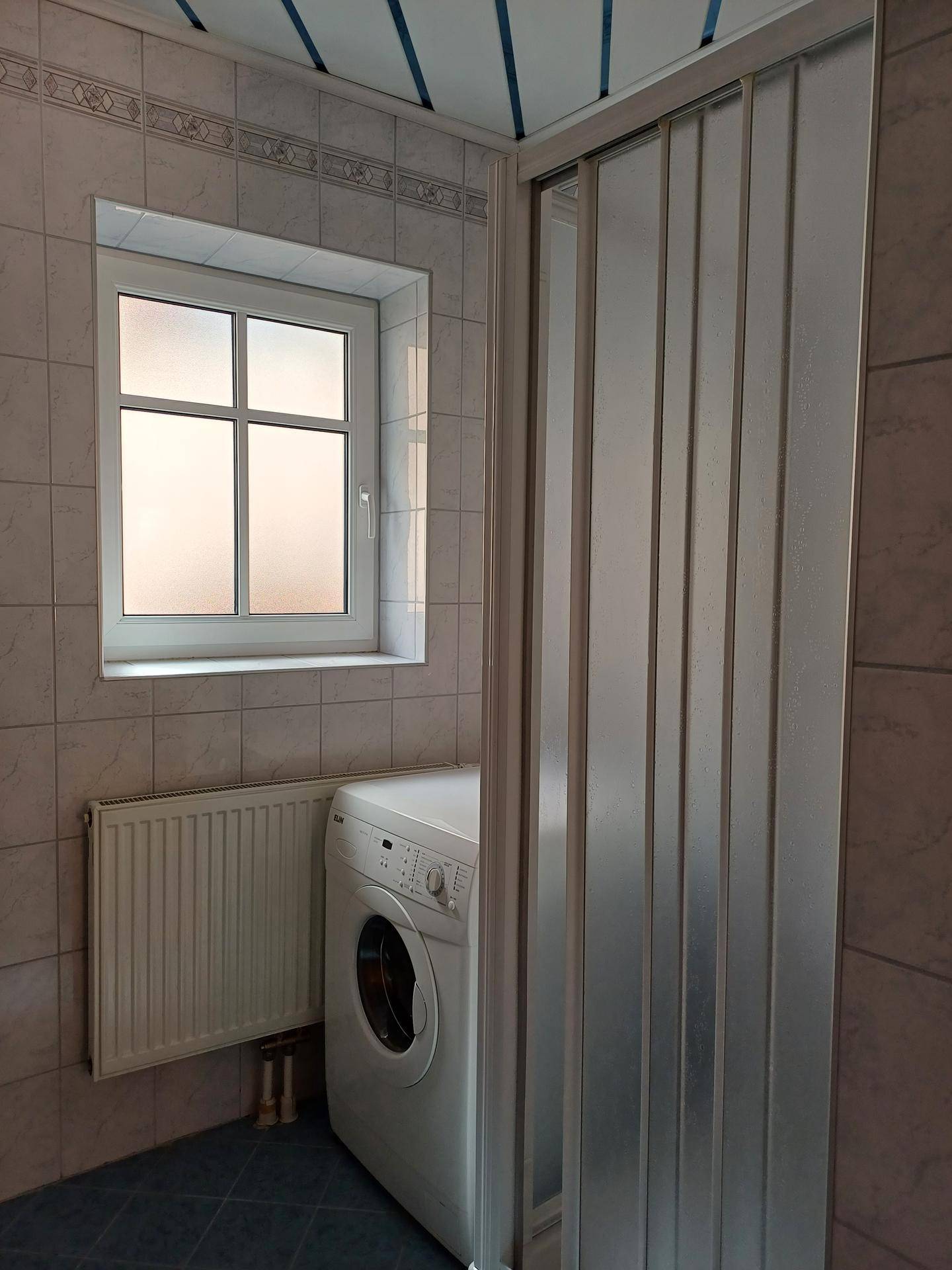 Badezimmer mit Duschkabine, Waschmaschine und Fenster für natürliche Belüftung.