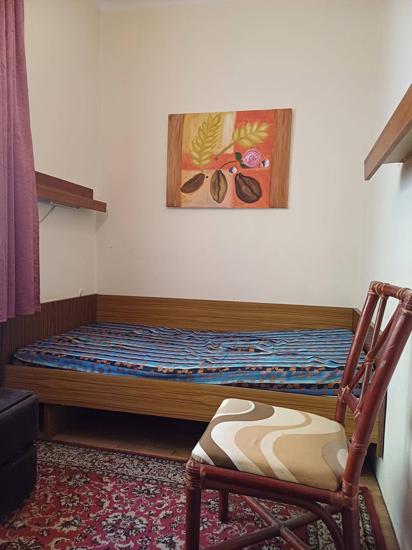 Schlafzimmer mit Einzelbett, Holzregalen und Teppichboden in warmen Farben.