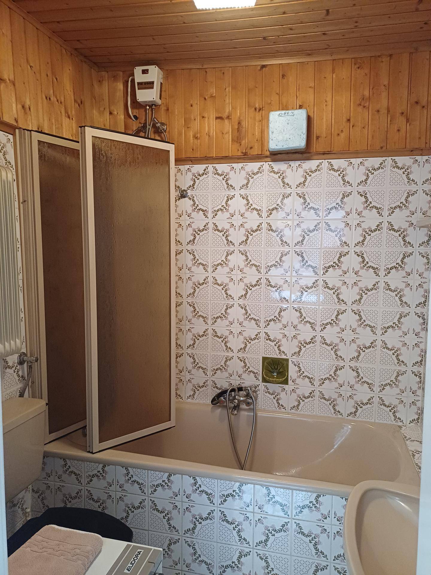 Badezimmer mit Badewanne, Duschabtrennung und holzverkleideter Decke.