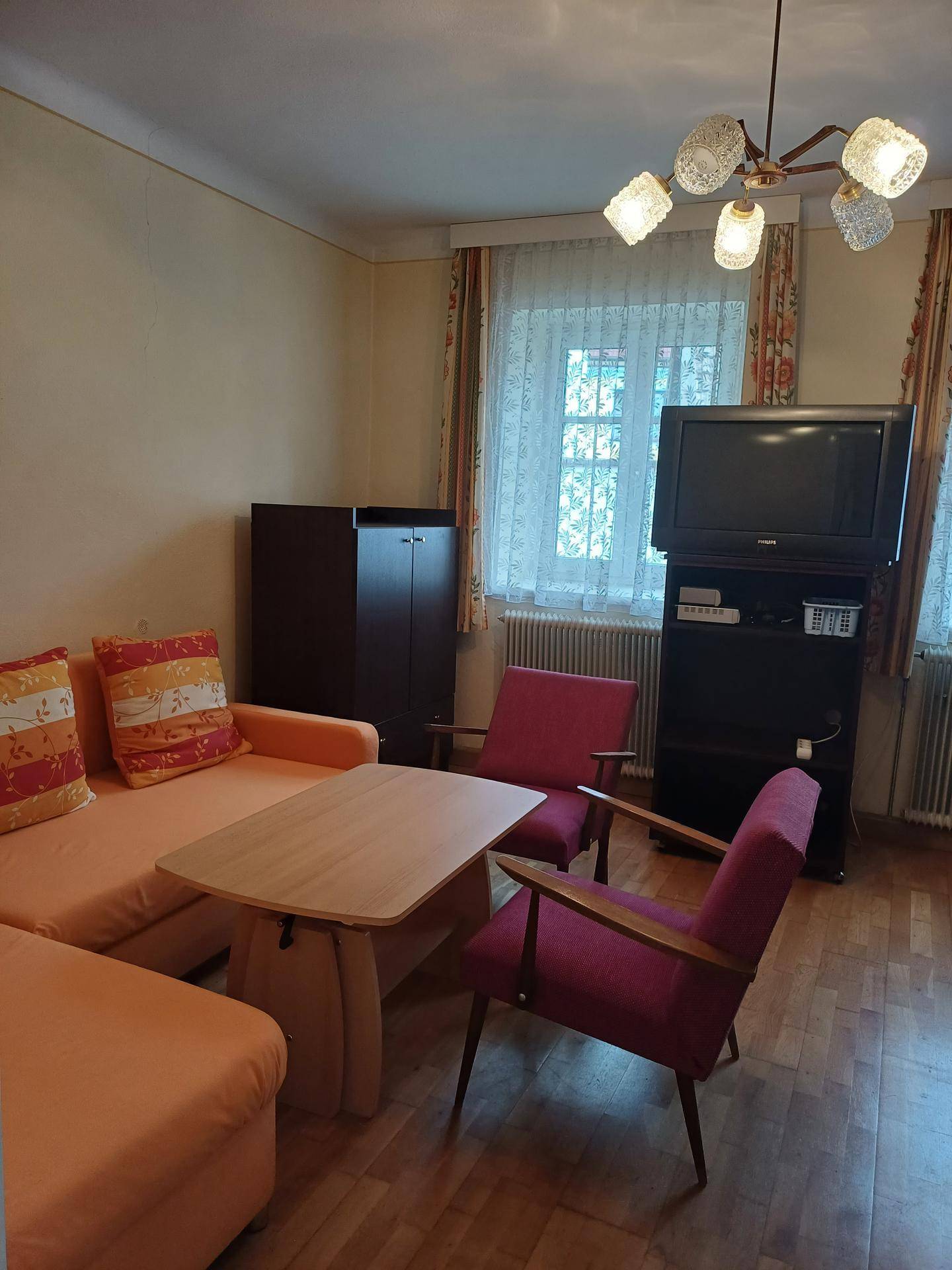 Wohnzimmer mit orangefarbenem Sofa, zwei Sesseln und einem Fernseher.