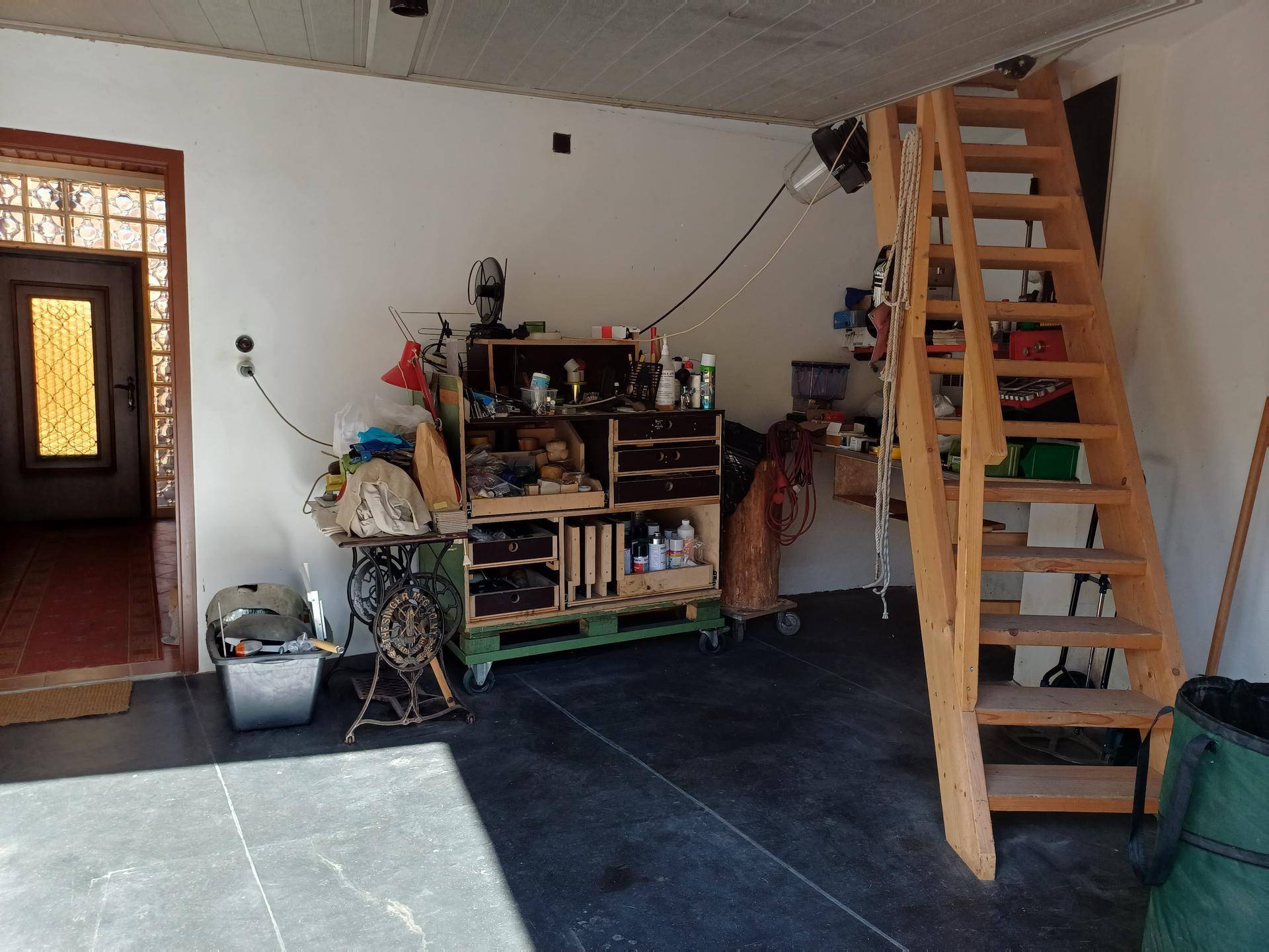 Werkstattraum mit Werkbank, Regalen und Holztreppe zum oberen Bereich.