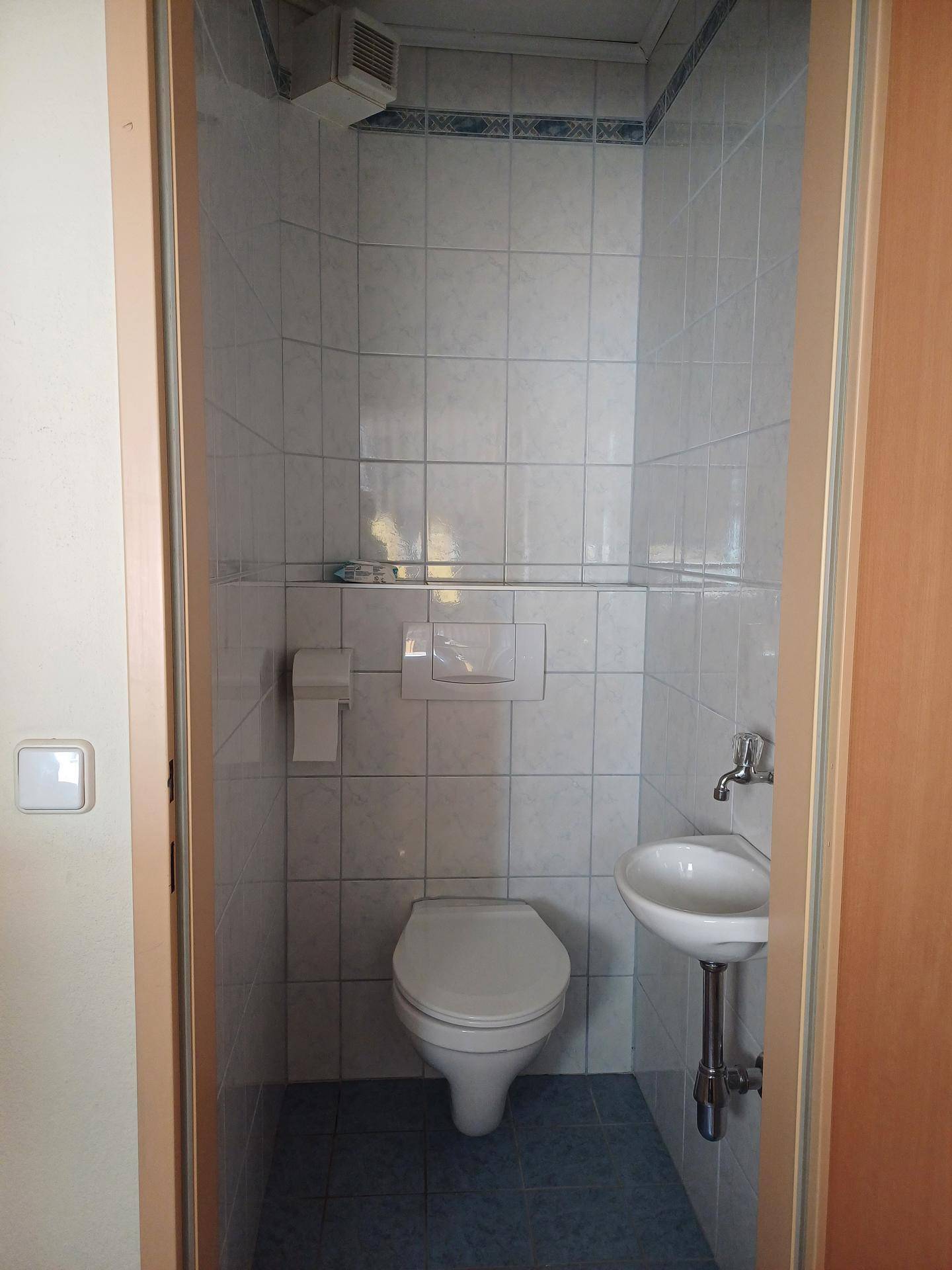 Kleines Gäste-WC mit Wand-WC, kleinem Waschbecken und hellen Fliesen.