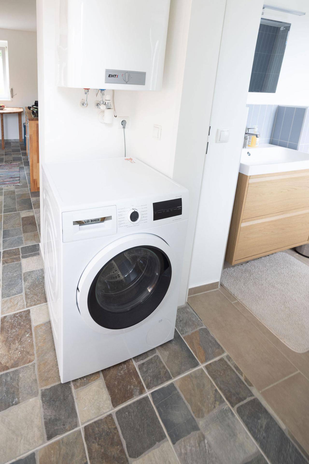 Waschmaschine und Warmwasserboiler in einem praktischen Hauswirtschaftsraum mit Fliesenboden.