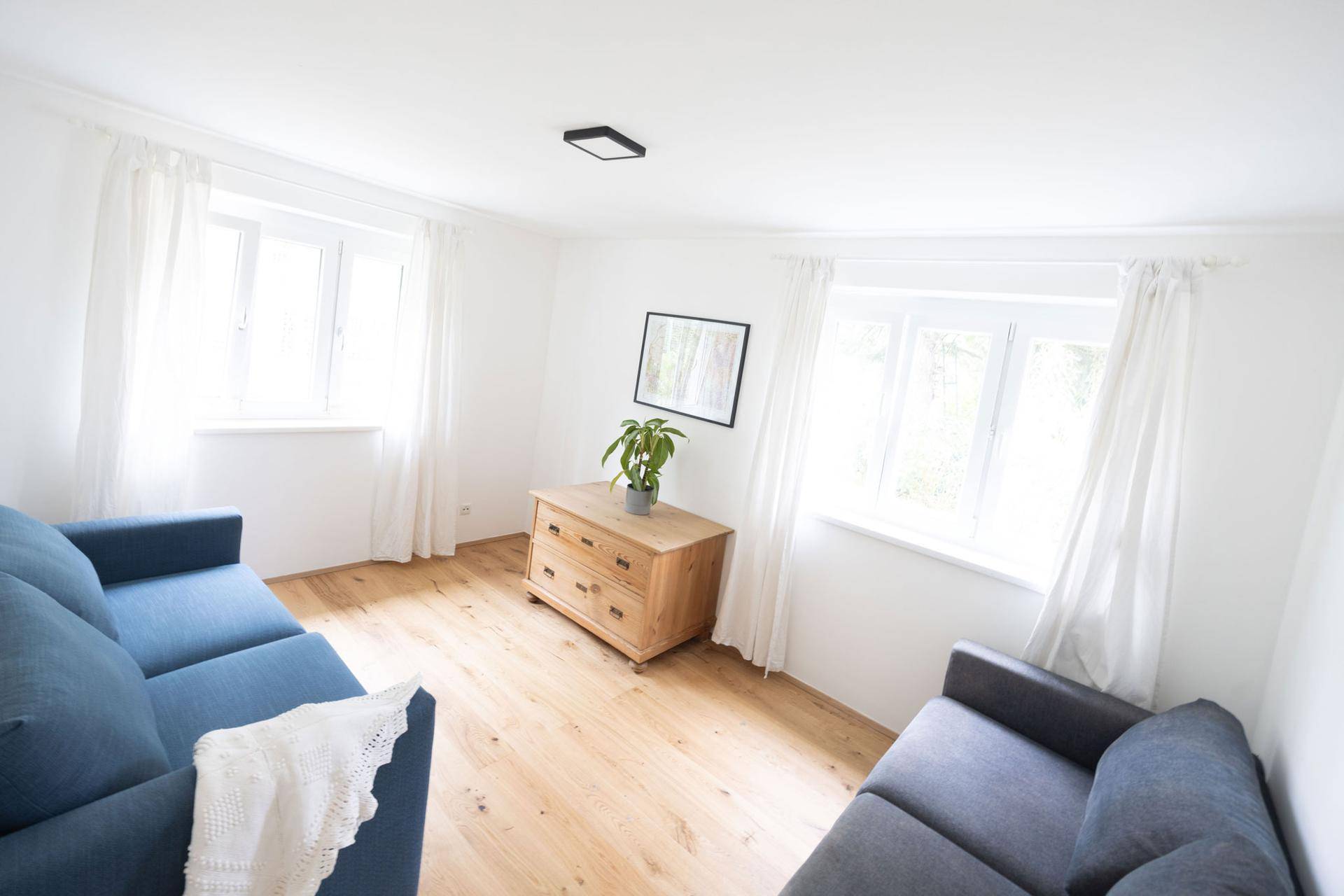 Helles Wohnzimmer mit zwei blauen Sofas, Holzkommode und schönem Holzfußboden.