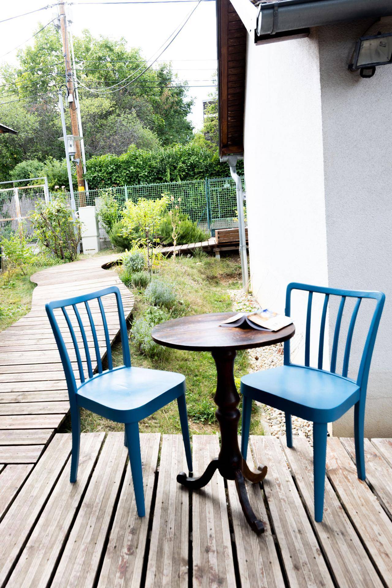 Gemütlicher Sitzbereich auf einer Holzterrasse mit kleinem Tisch und zwei blauen Stühlen.