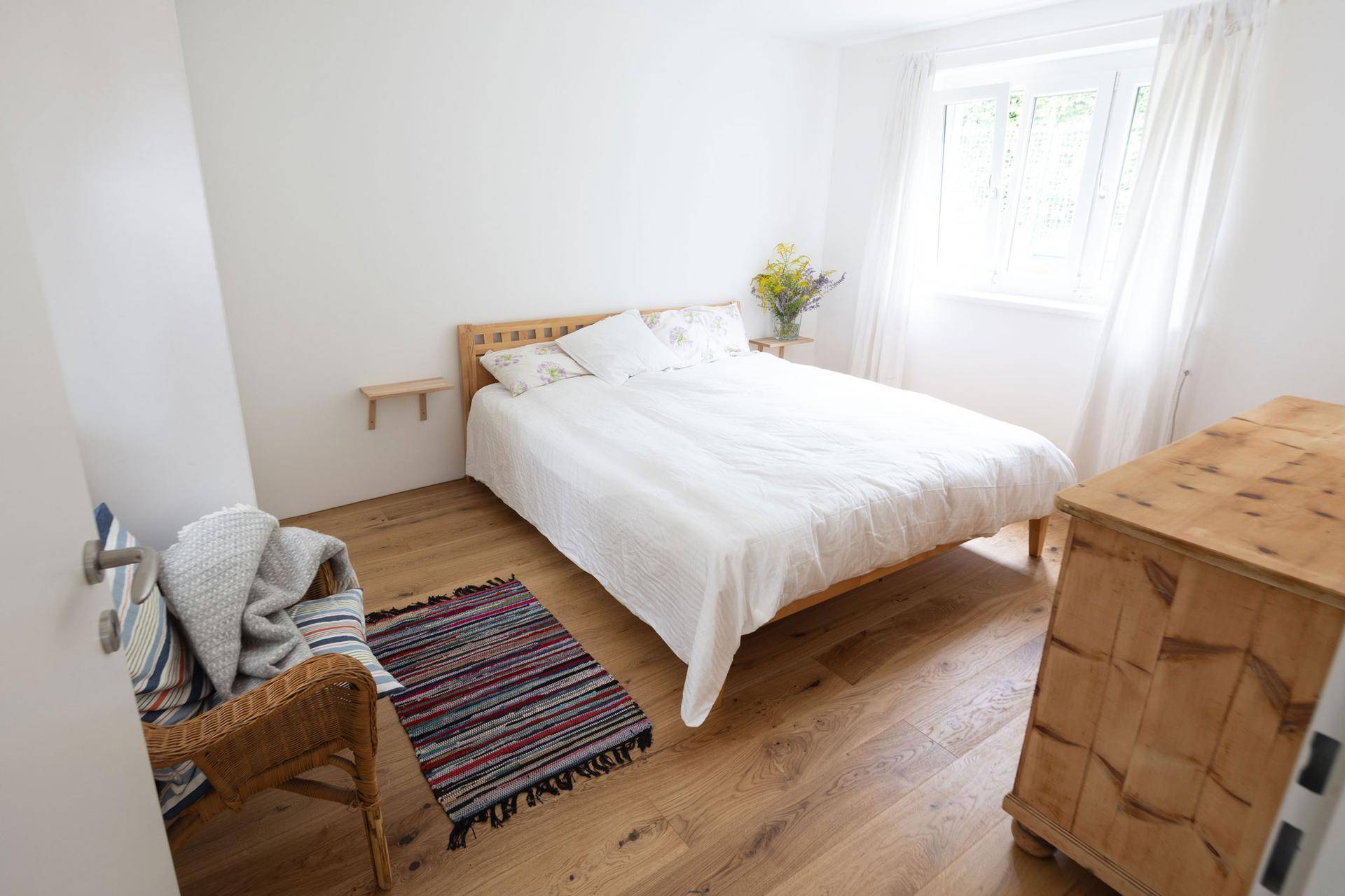 Helles Schlafzimmer mit Holzbett, weißer Bettwäsche und warmem Holzfußboden.