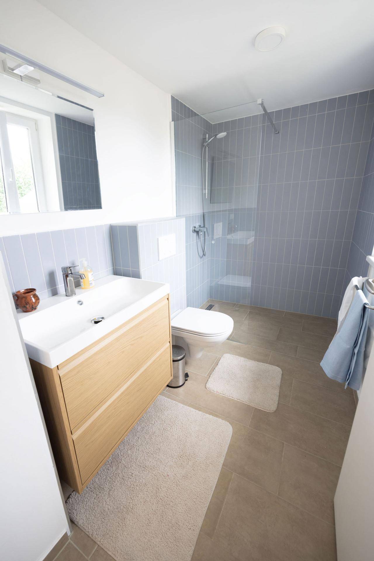Modernes Badezimmer mit hellblauen Fliesen, Holzwaschtisch und ebenerdiger Dusche.