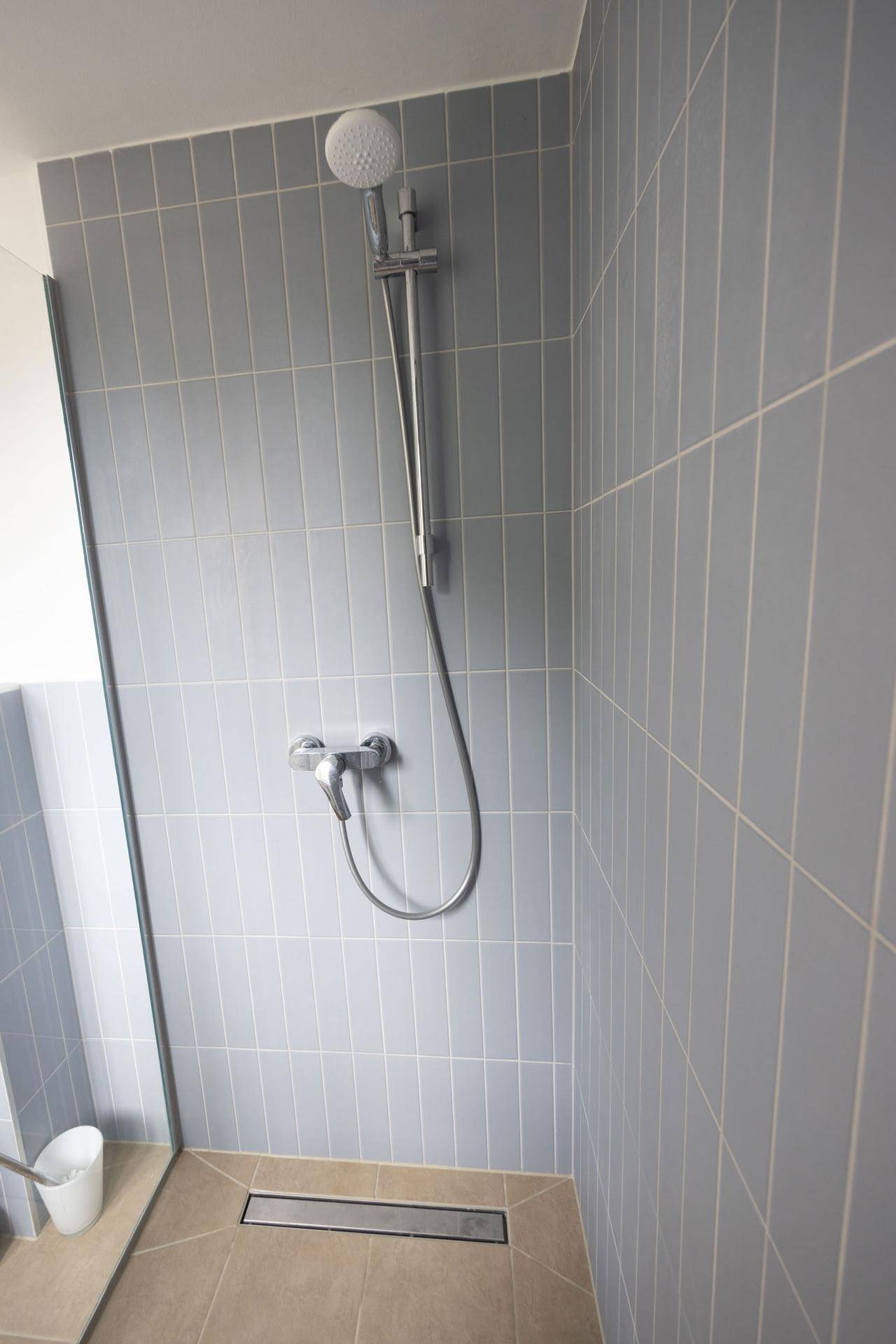 Ebenerdige Dusche mit hellblauen Fliesen und modernem linearem Abfluss im Badezimmer.