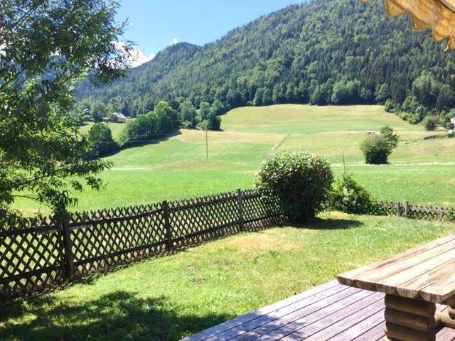 Weitläufiger Blick von der Holzterrasse über grüne Wiesen und bewaldete Berge in der Ferne.