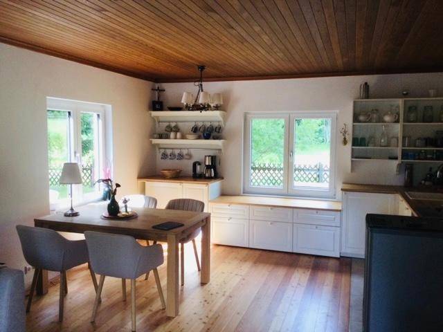 Helle Küche mit Essbereich, Holzboden und Holzdecke, weißen Schränken und Blick ins Grüne.