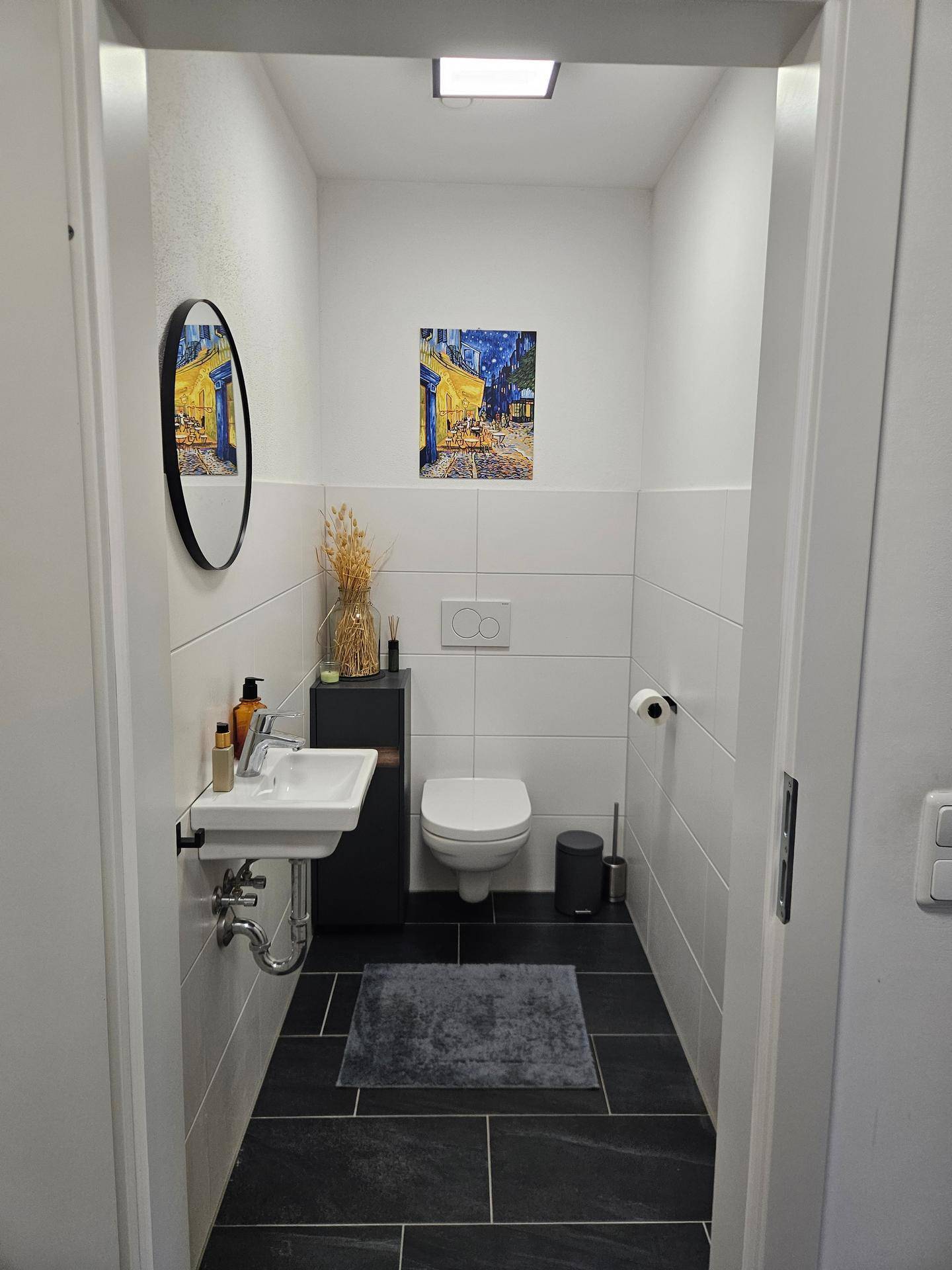 Modernes Gäste-WC mit Wand-WC, kleinem Waschbecken und dunklen Fliesen.