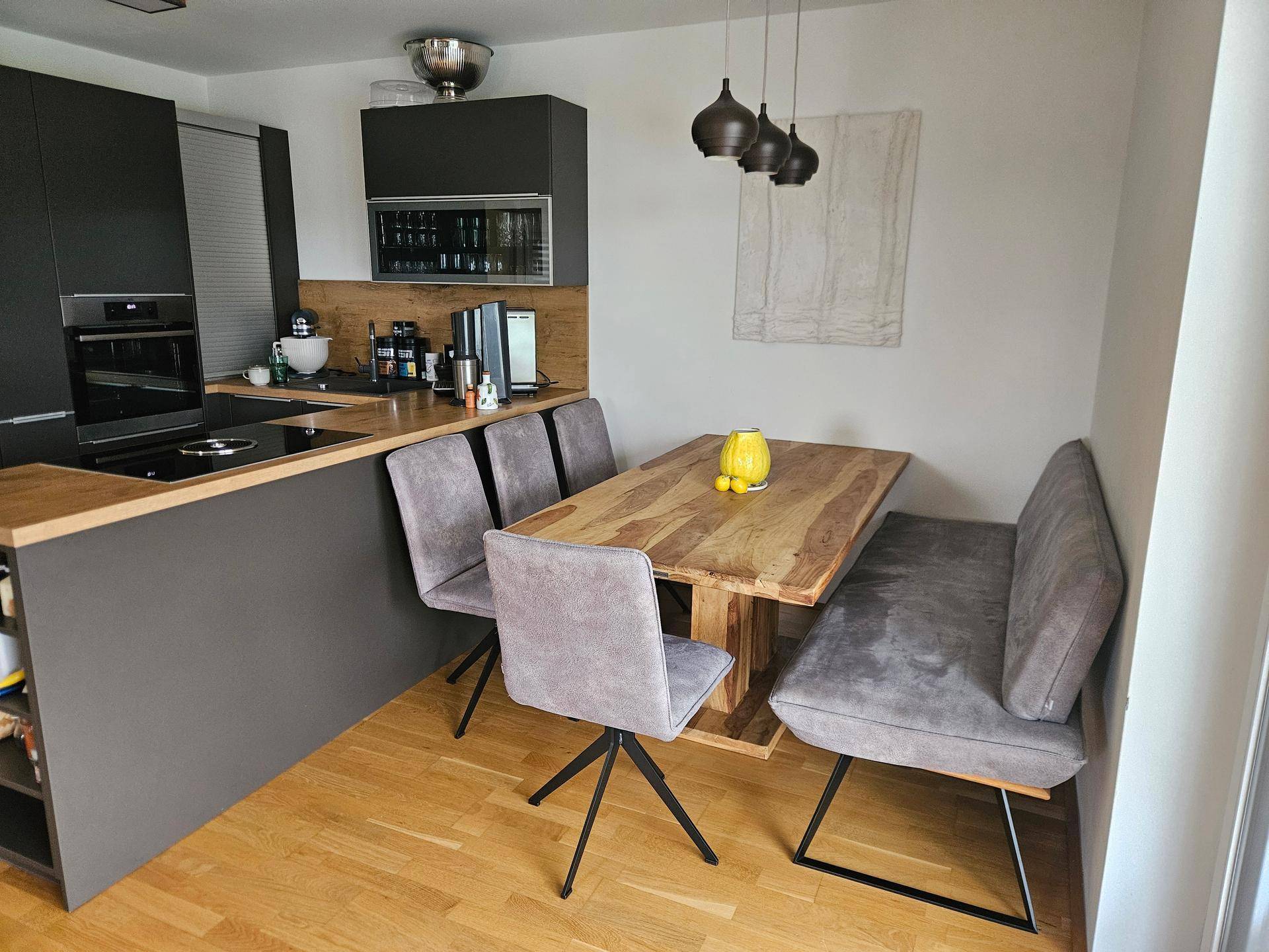 Essbereich in der Küche mit Holztisch, Sitzbank und modernen Pendelleuchten.