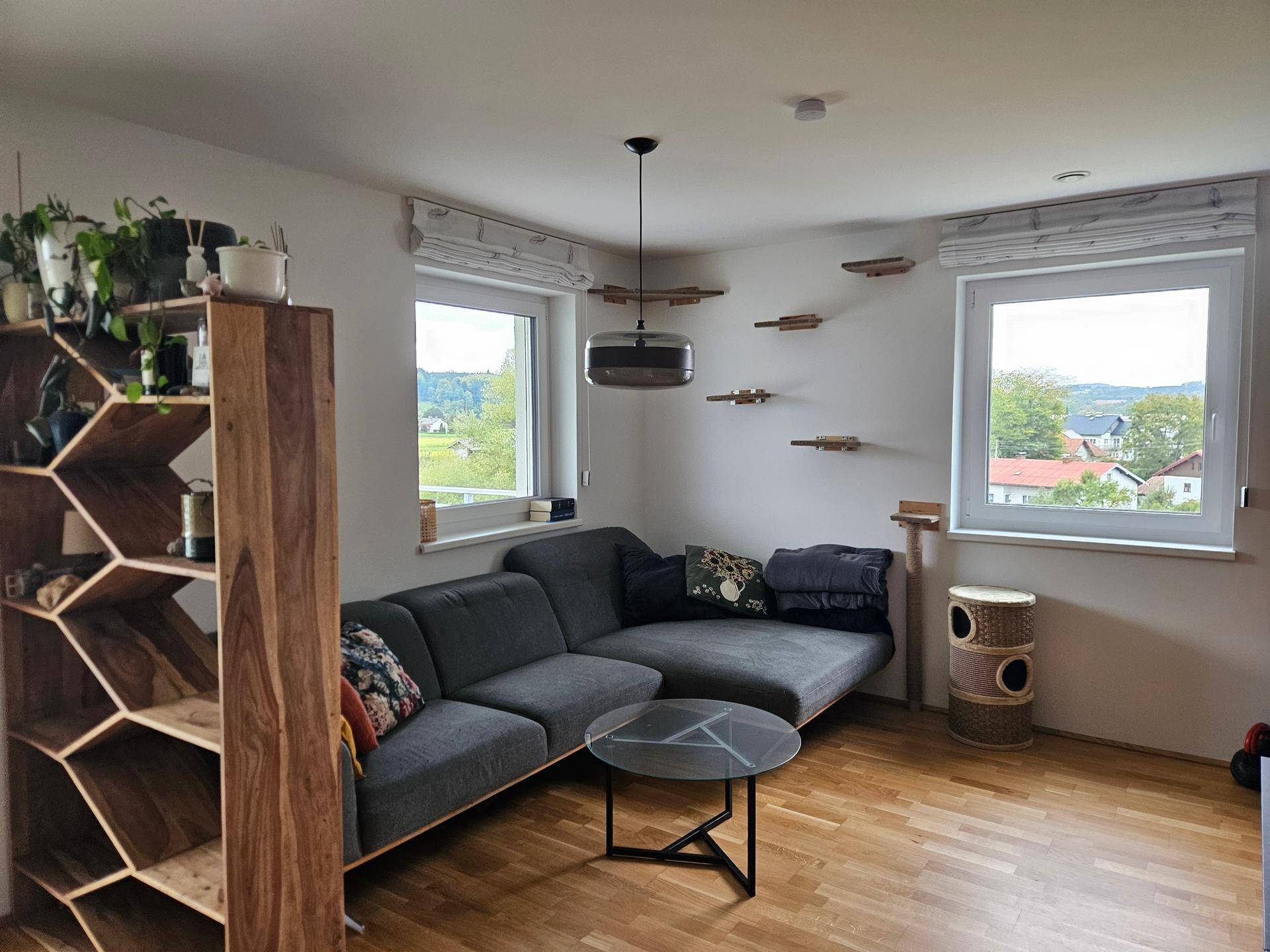 Gemütliches Wohnzimmer mit Ecksofa, Holzboden und Blick in die Landschaft.
