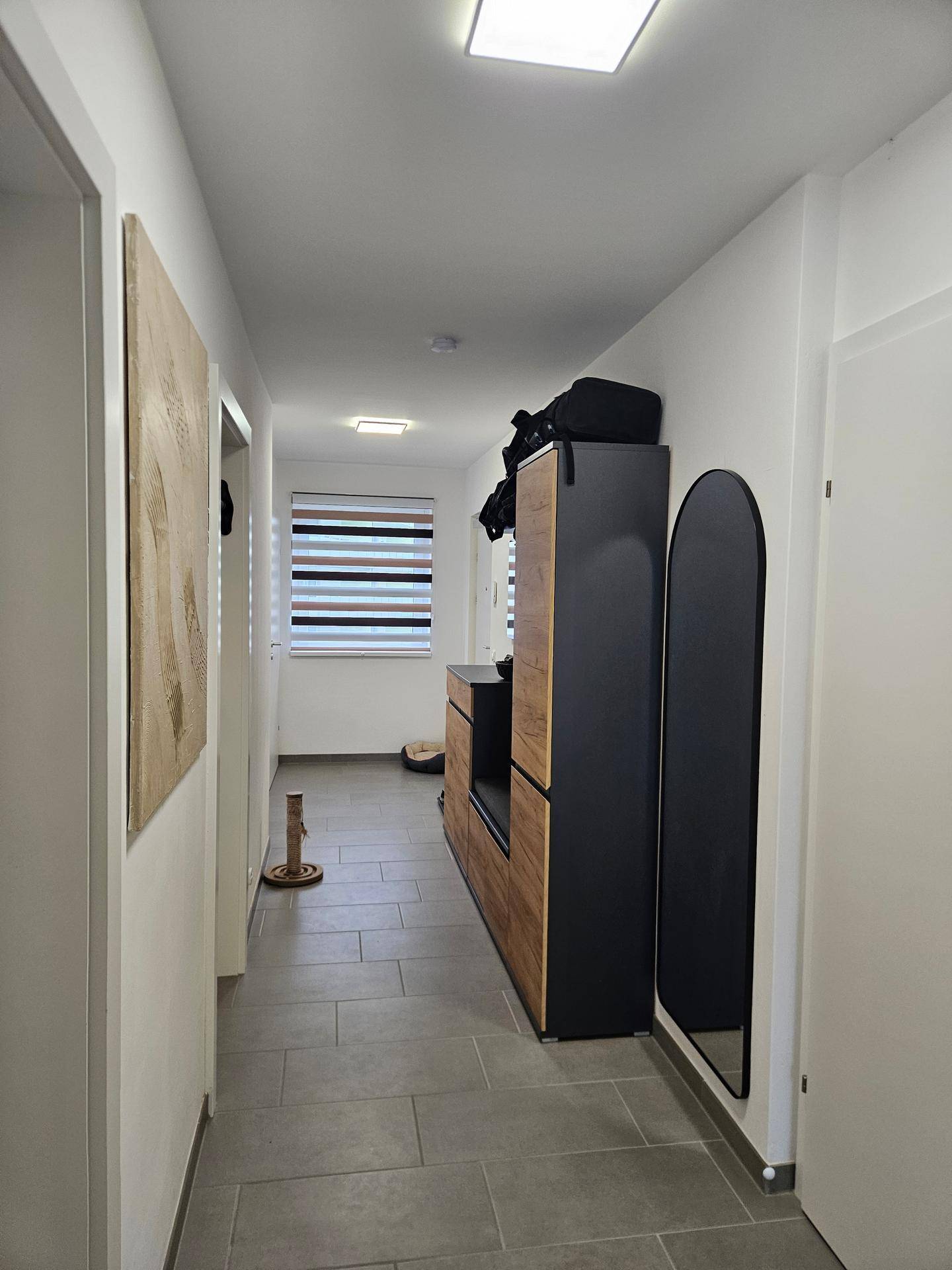 Heller Flur mit Fliesenboden, Garderobe und Blick zum Fenster.