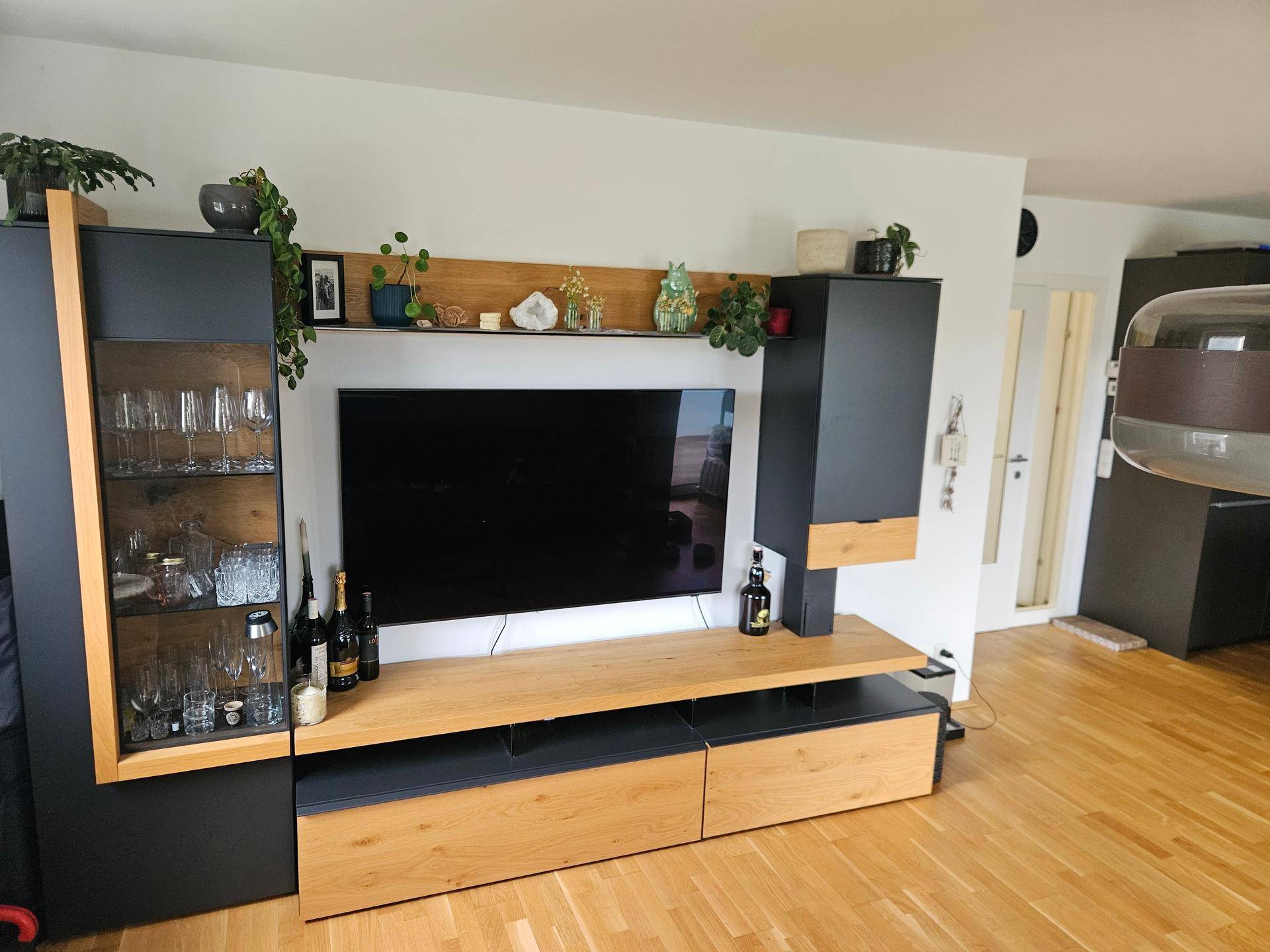 Wohnzimmer mit großem Fernseher, modernen Möbeln und Holzboden.