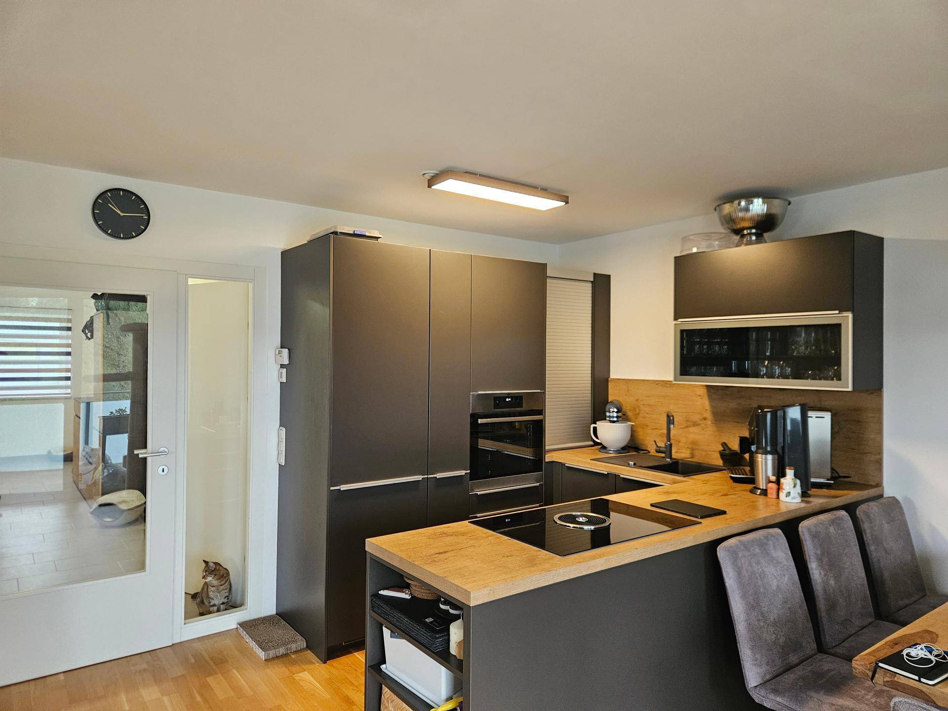 Moderne Küche mit dunklen Schränken, Holztheke und integrierten Geräten.