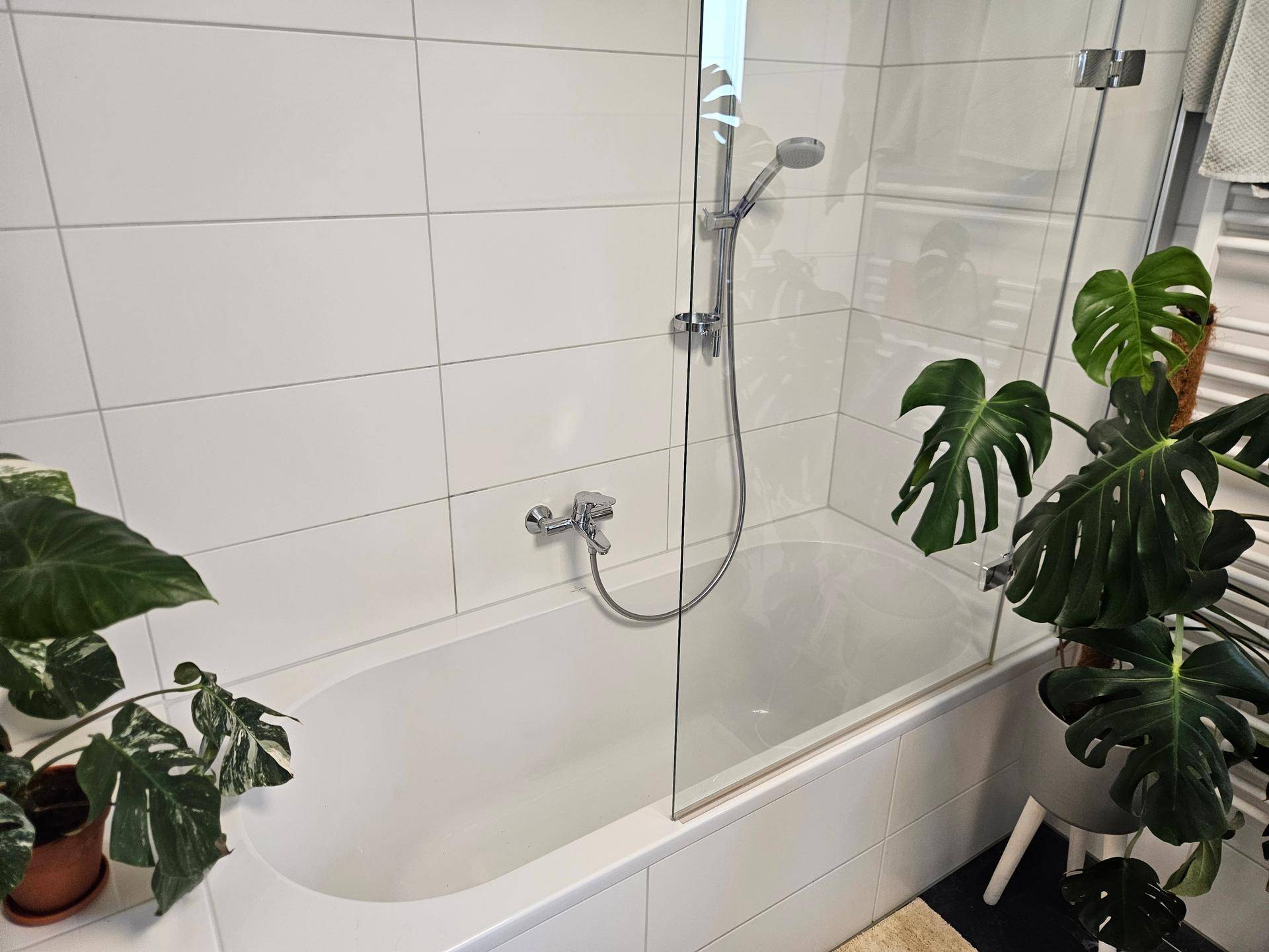 Badewanne mit Duschabtrennung aus Glas in einem hell gefliesten Badezimmer.