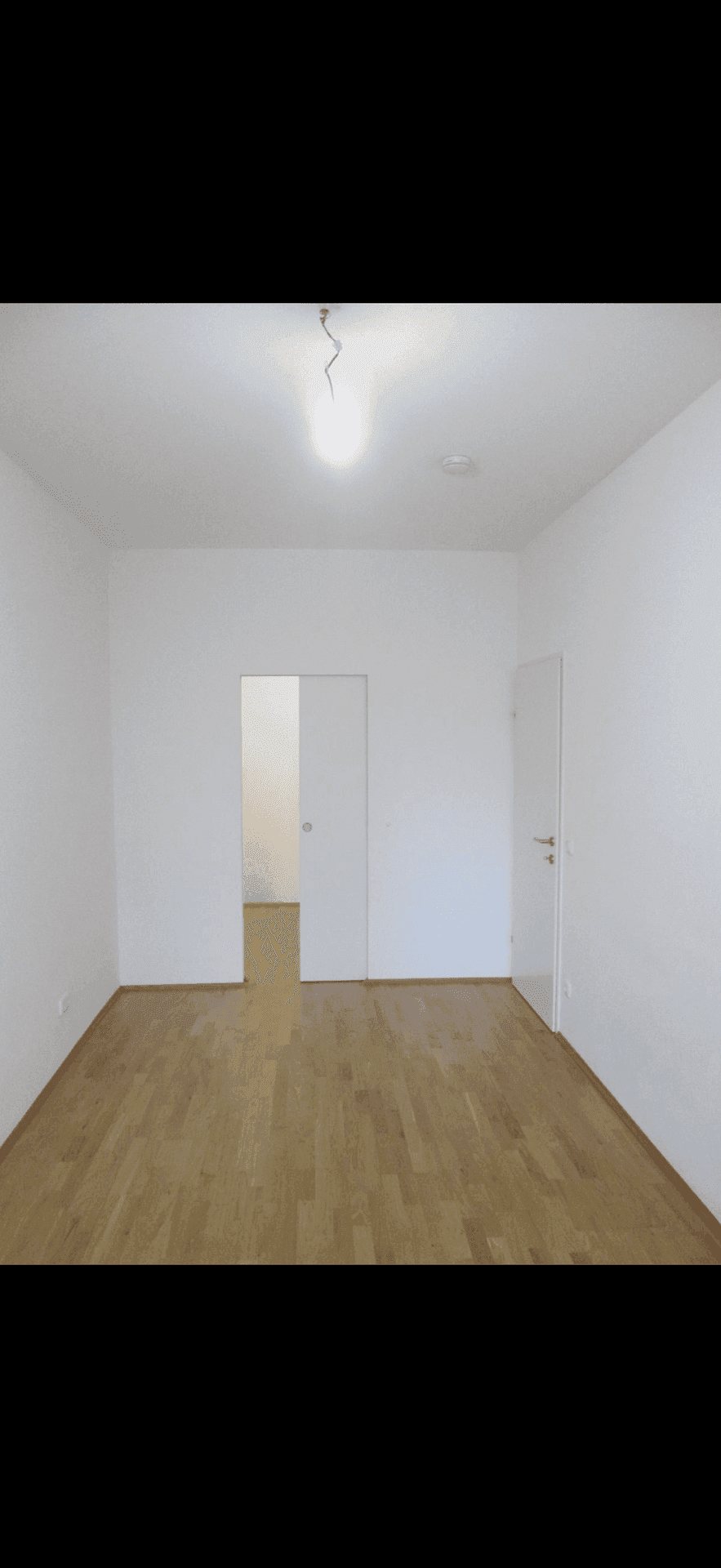 Helles, leeres Zimmer mit Holzboden und einer modernen Schiebetür zu einem weiteren Raum.