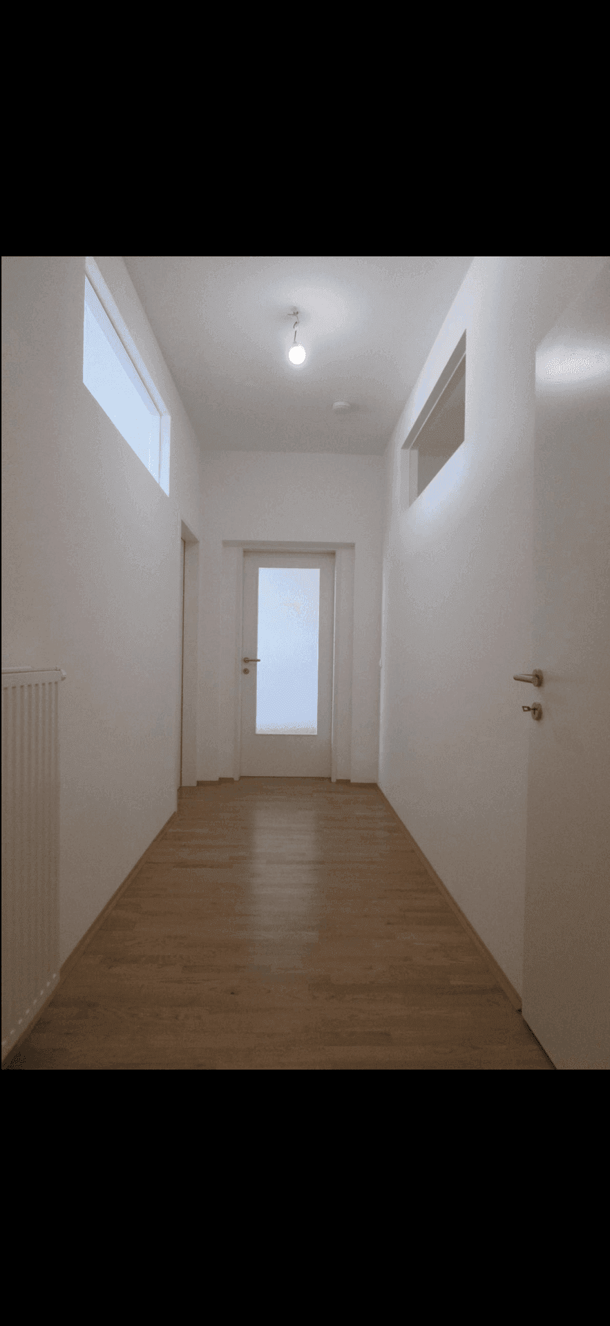 Heller Flur mit Holzboden, weißen Wänden und Türen, der zu verschiedenen Räumen führt.