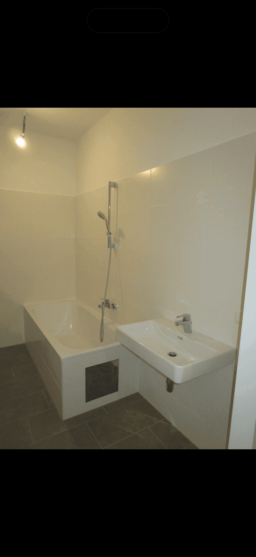 Modernes Badezimmer mit Badewanne, Waschbecken und hellen Fliesen an Wänden und Boden.